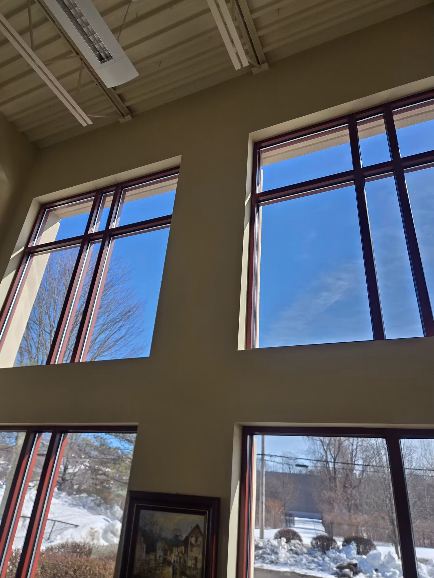 Tall commercial lobby windows with tinted glass reducing heat and glare from the bright winter sky.