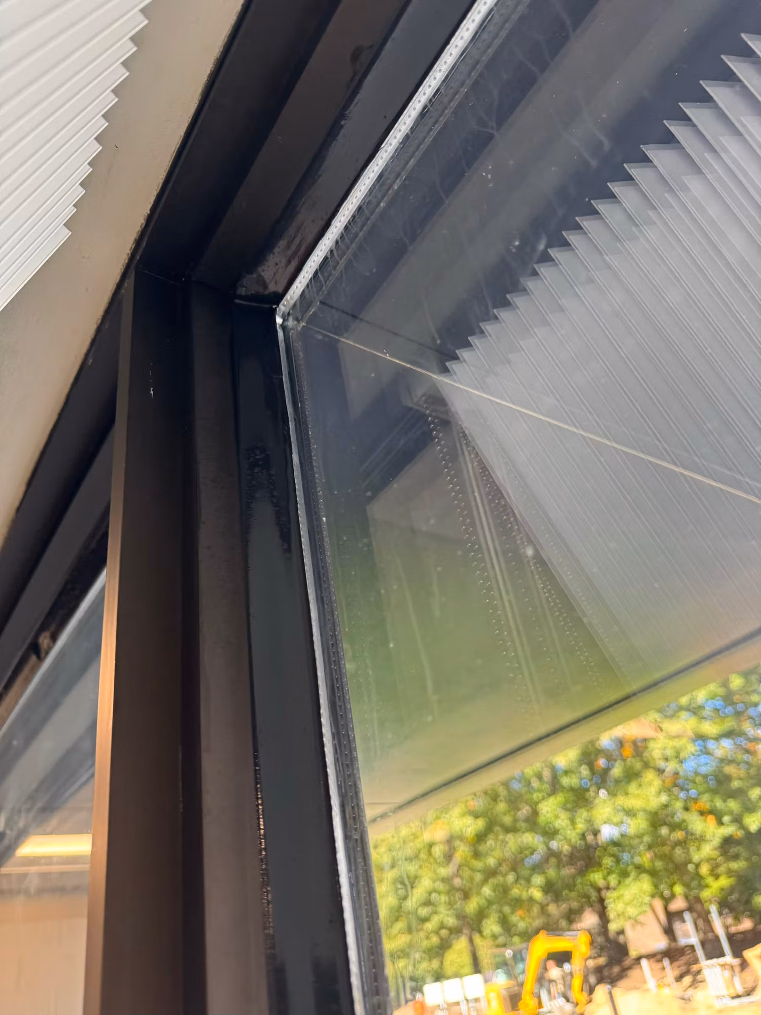 Upper corner of a dark-framed office window with freshly installed window film and a pleated shade alongside.