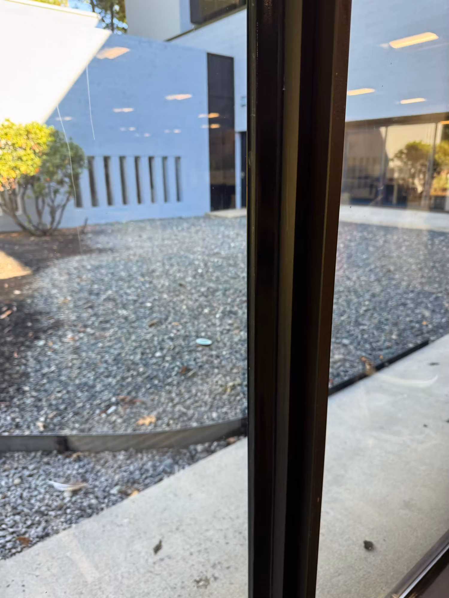 Large commercial office window overlooking a gravel courtyard and white building exterior beyond a dark mullion.