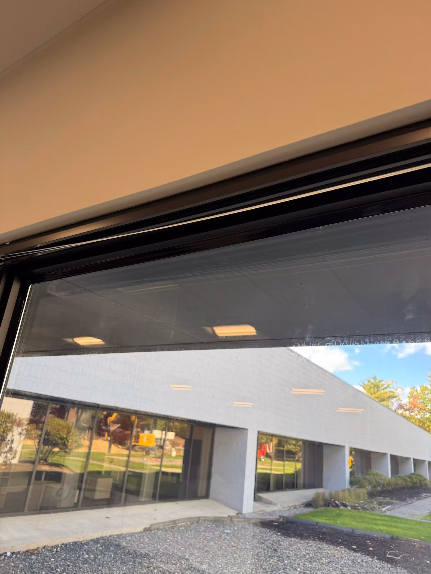 Large office floor-to-ceiling window with a dark solar screen, overlooking a low white brick building and grounds.
