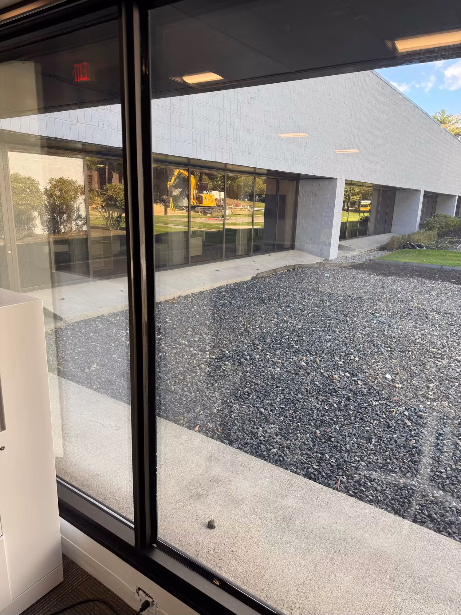 Commercial glass door and window overlooking the building exterior and gravel grounds with an excavator outside.