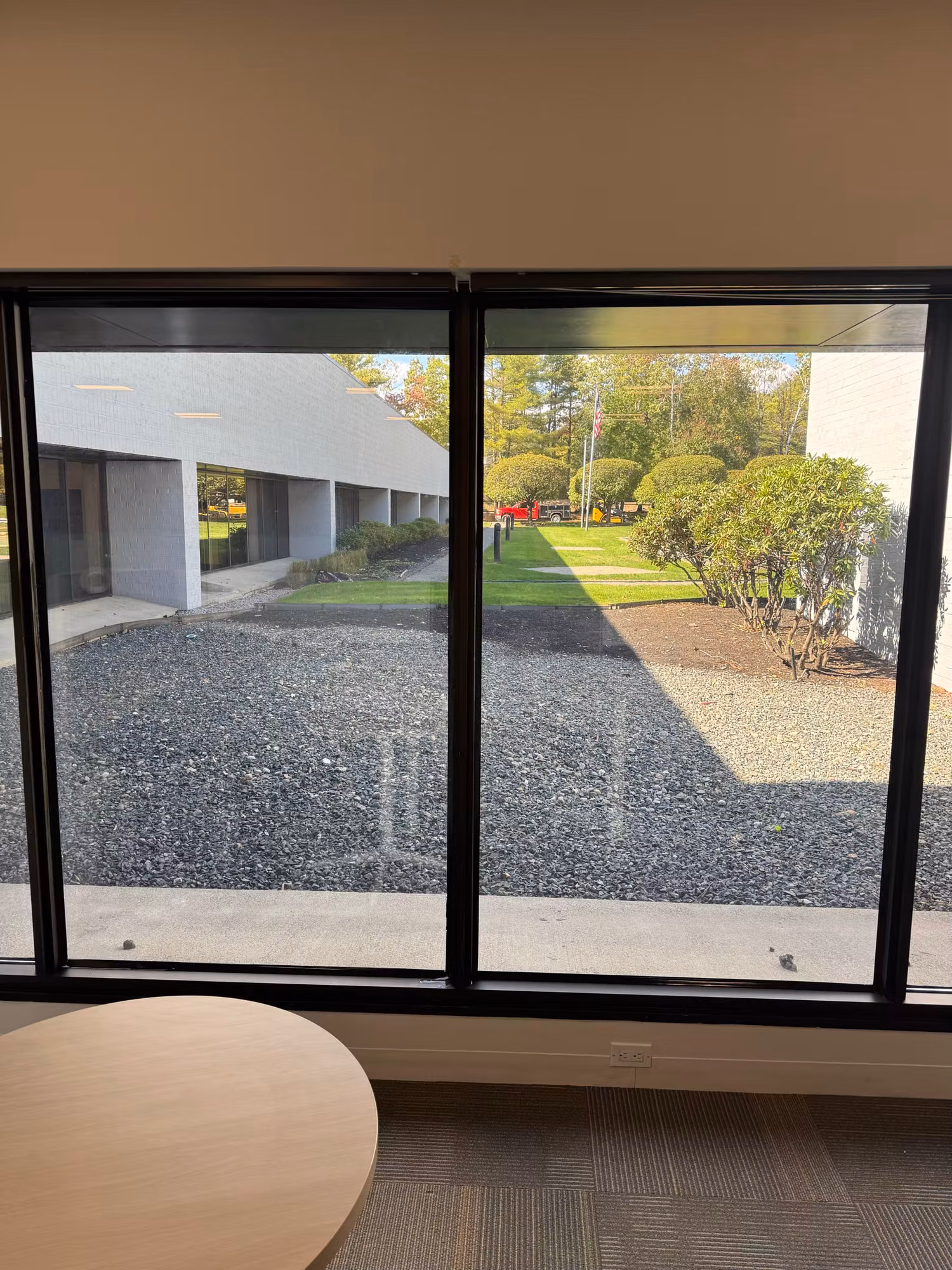 Interior office picture windows framing a view of the courtyard and grounds, with a round table nearby.