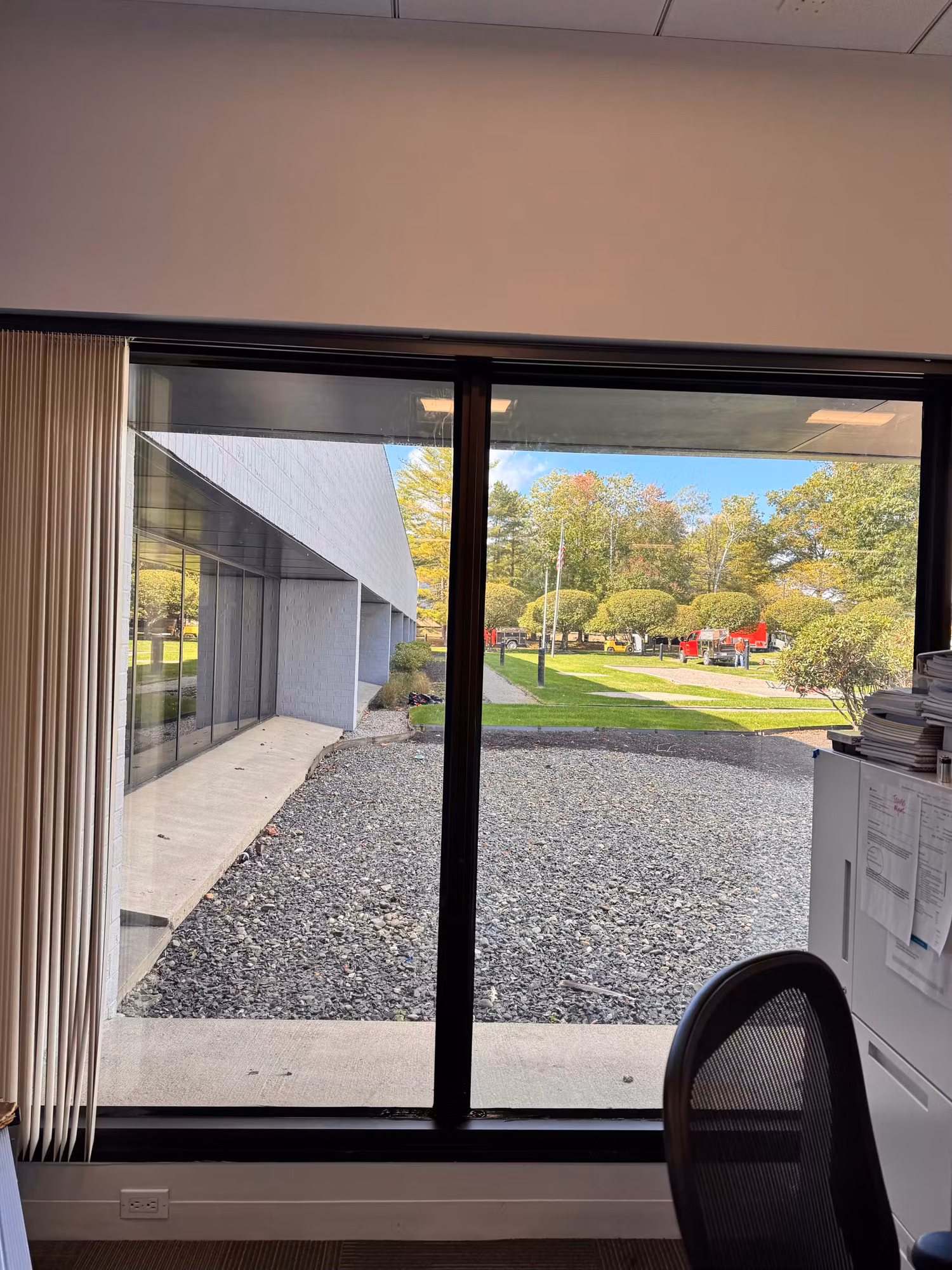 Private office with a large tinted picture window and curtains overlooking a landscaped courtyard.