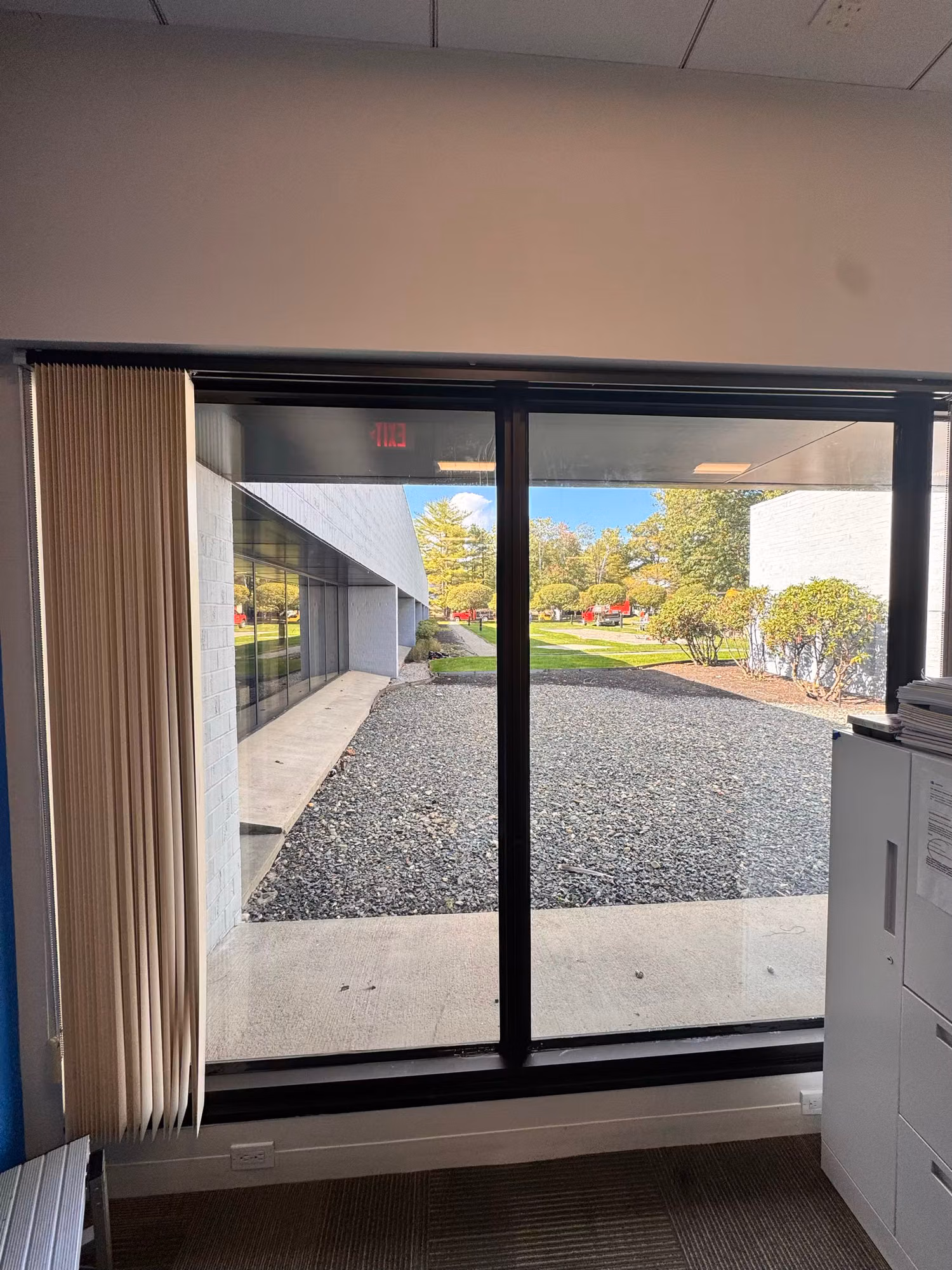 Office interior with a large tinted sliding window and curtains looking out onto a gravel courtyard.