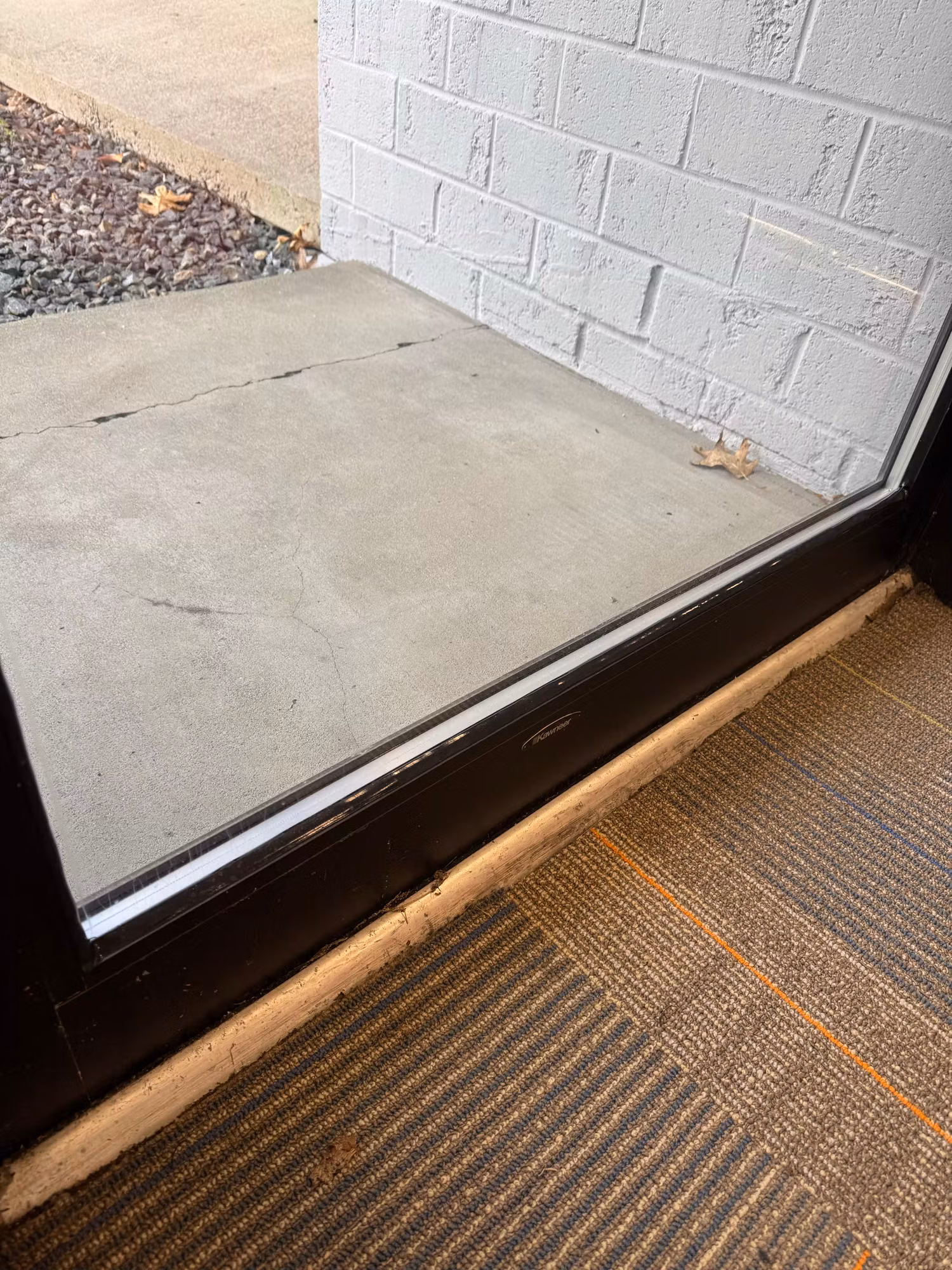 Lower edge of a commercial storefront glass door at the threshold beside concrete and carpet tile flooring.