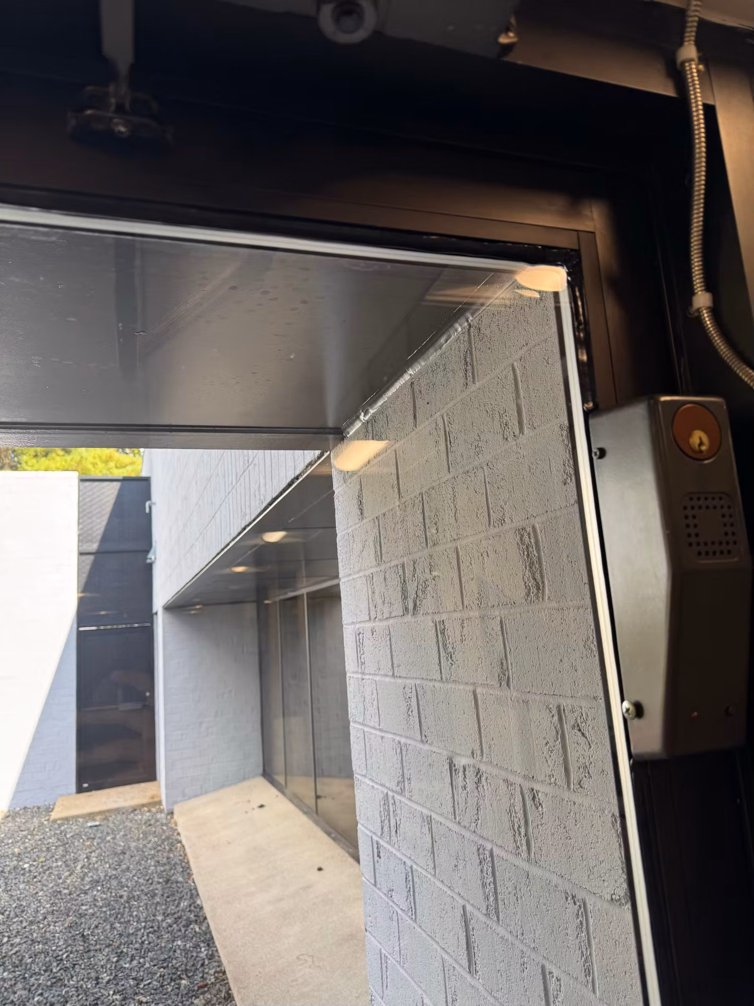 Top corner of a glass storefront door with an electronic lock beside a painted brick wall.
