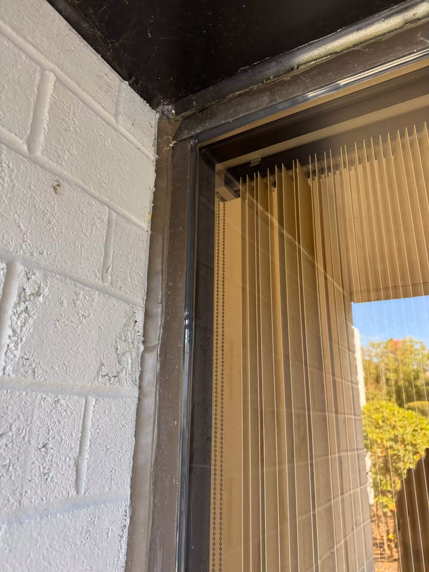 Commercial storefront window with vertical blinds inside, framed beside a painted brick exterior wall corner.