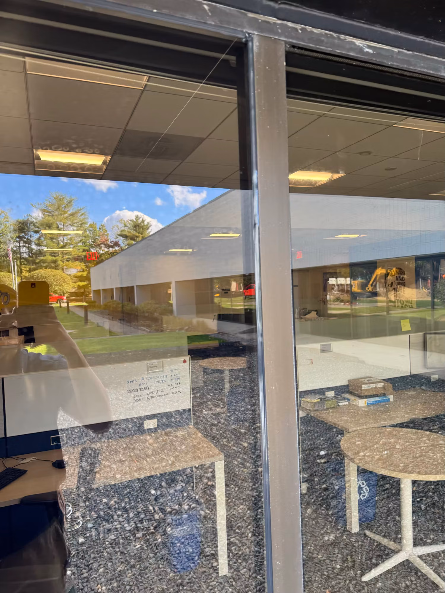 Commercial storefront glass revealing an office break area with tables and chairs while reflecting the grounds outside.
