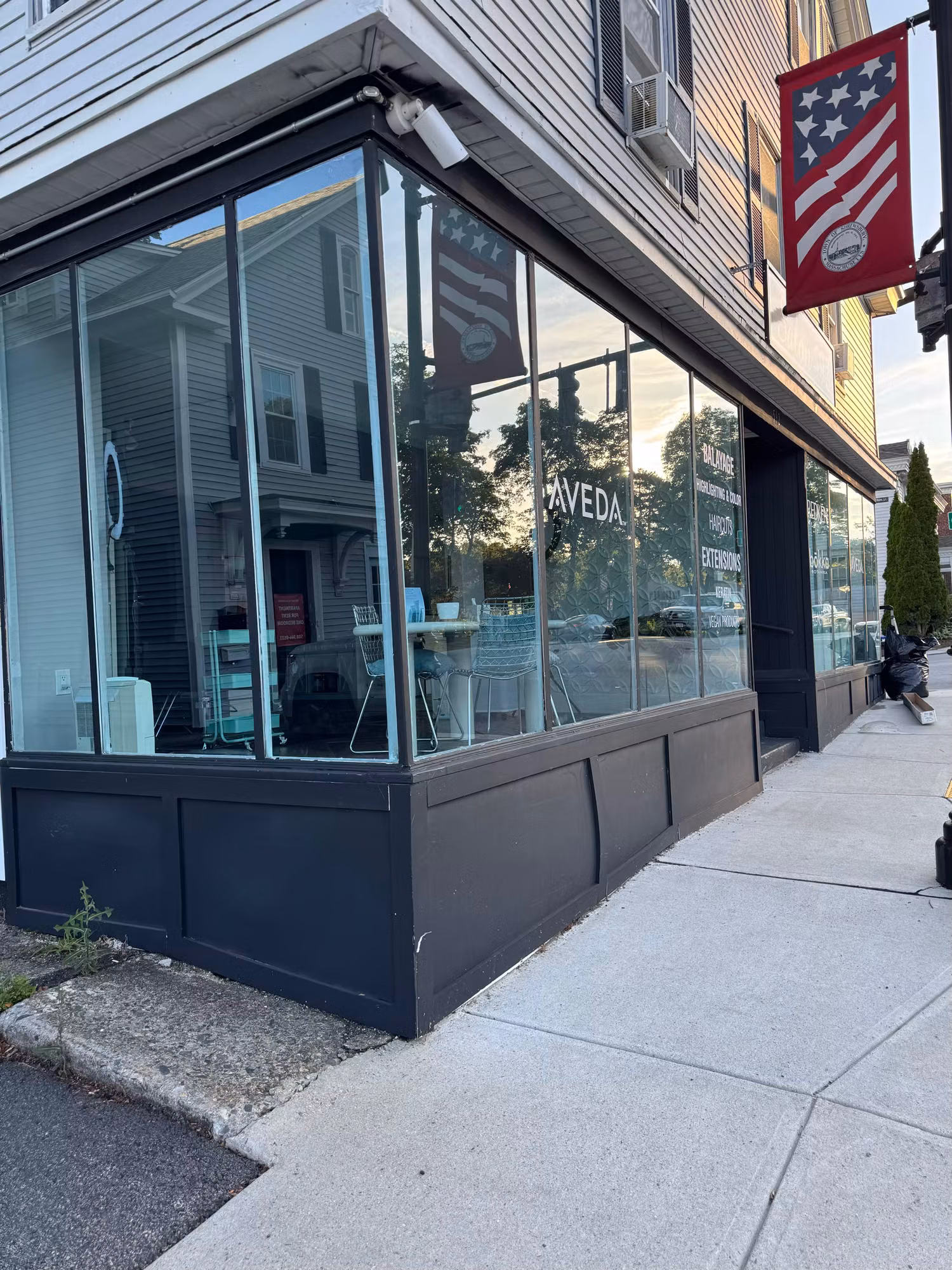 Corner salon display window with applied white vinyl branding and lettering across the large storefront glass.