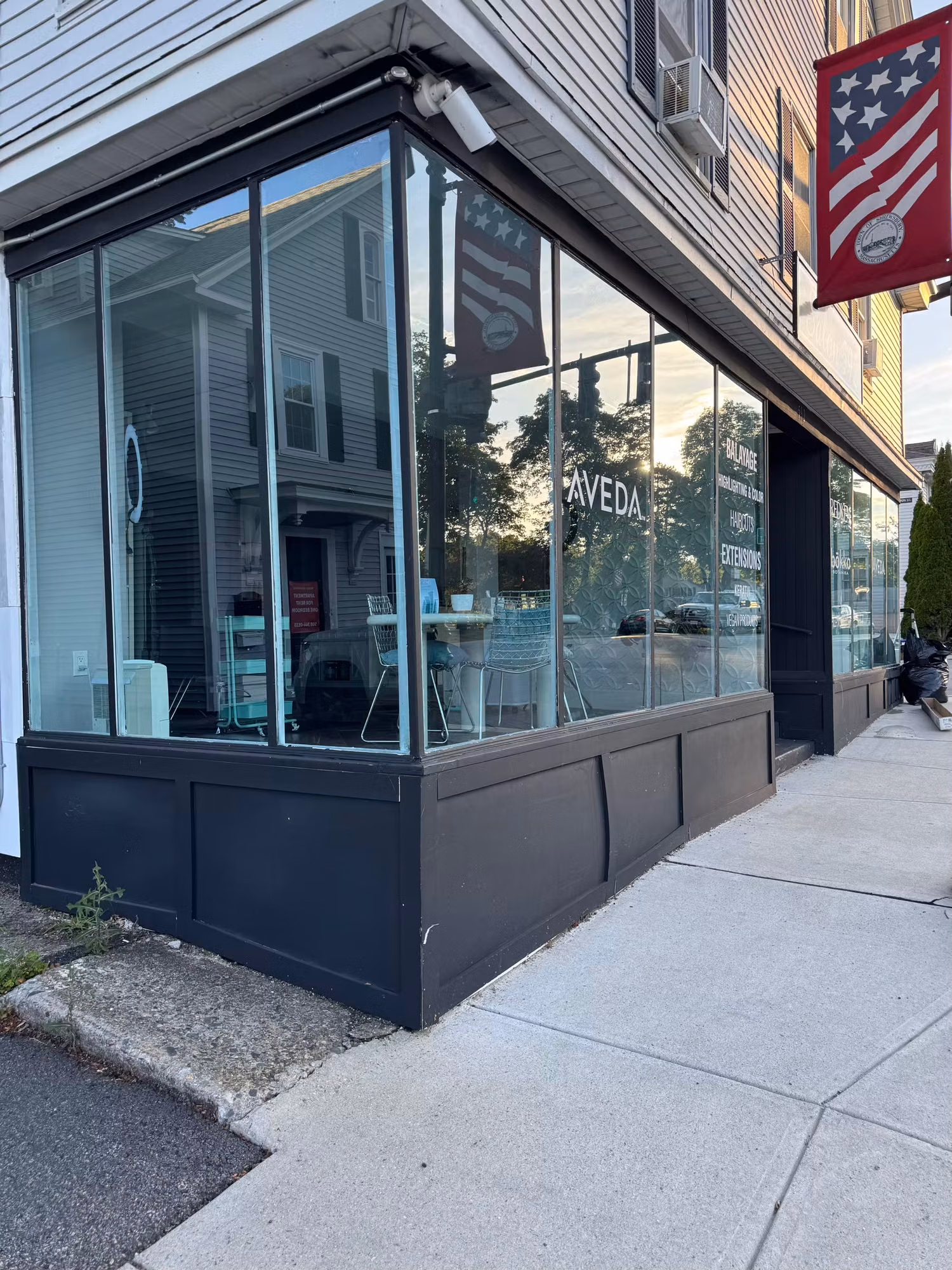 Large corner storefront window of a salon with vinyl brand lettering applied to the glass at dusk.