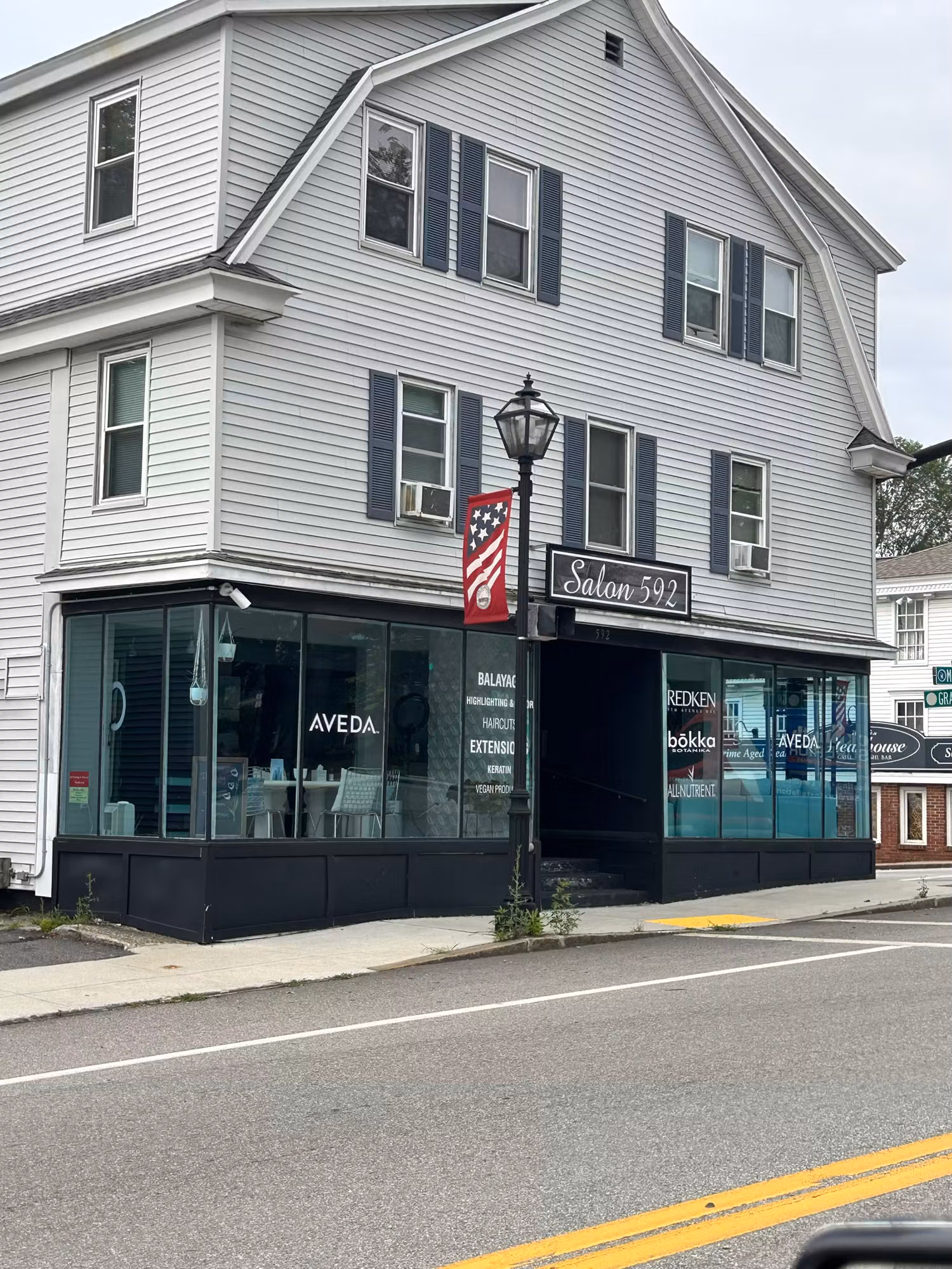 Two-story corner salon with wraparound storefront windows displaying white vinyl lettering and brand graphics on the glass.