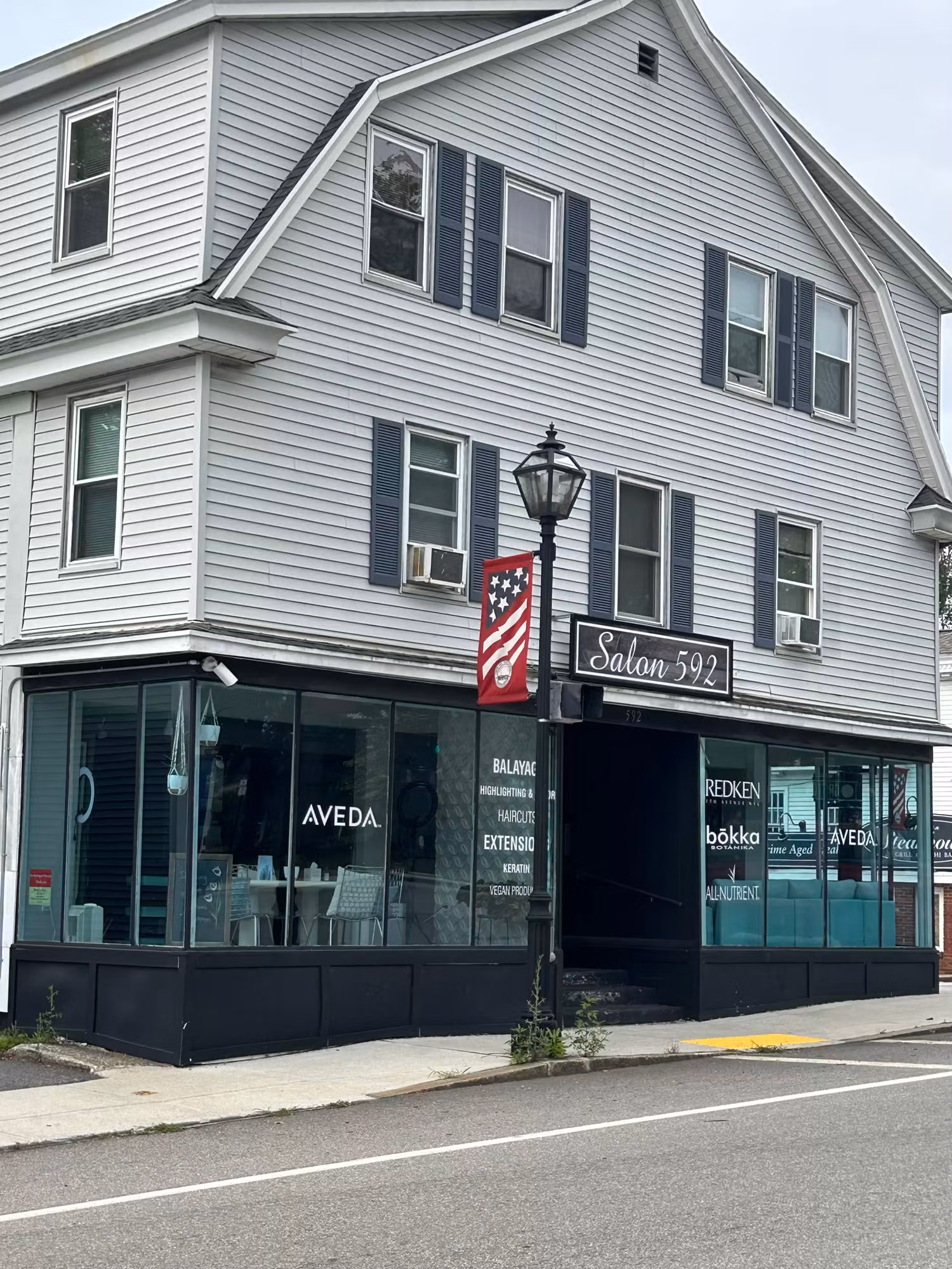 Salon exterior at the corner with wraparound display windows carrying white vinyl service lettering on the glass.
