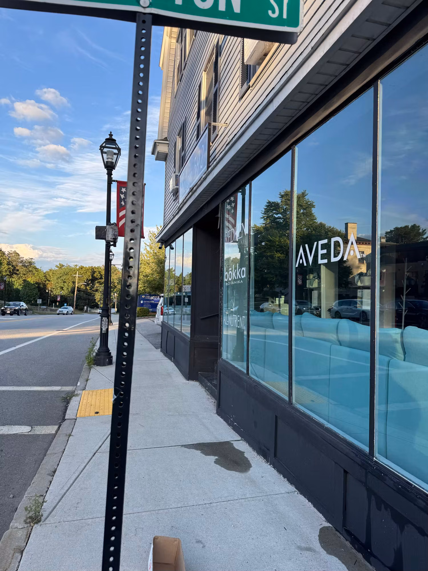 Sidewalk view of a salon storefront with floor-to-ceiling tinted windows reflecting the sky and street.