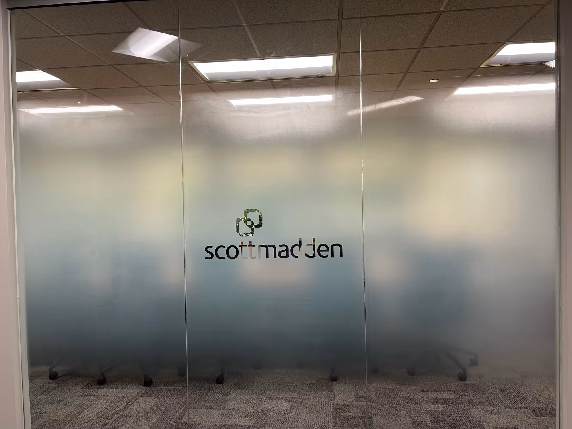 Glass partition wall with a gradient frosted privacy film and a clear cut-out logo centered on the panel.