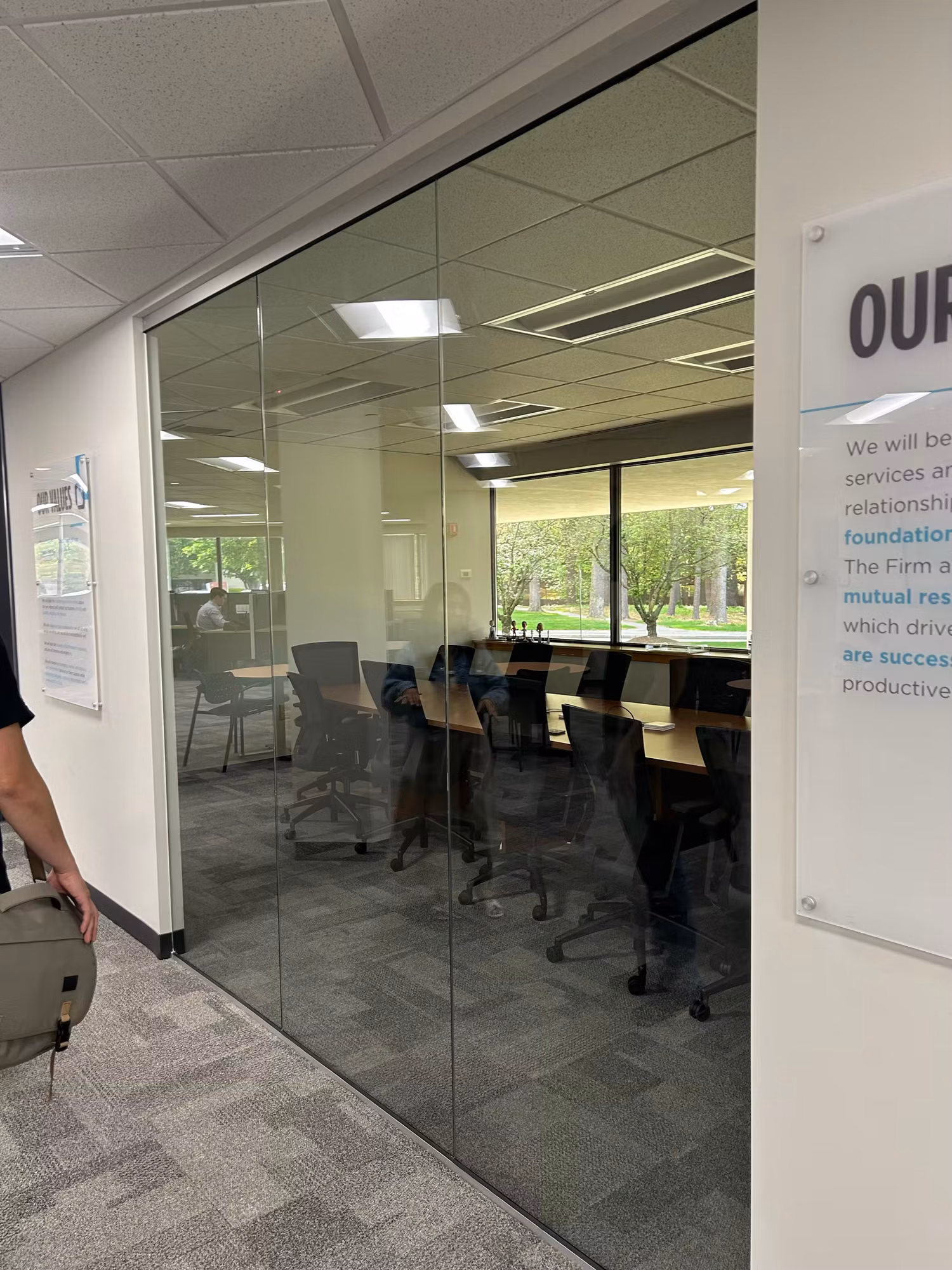 Glass-walled conference room with a meeting table and chairs, viewed through a floor-to-ceiling glass partition.