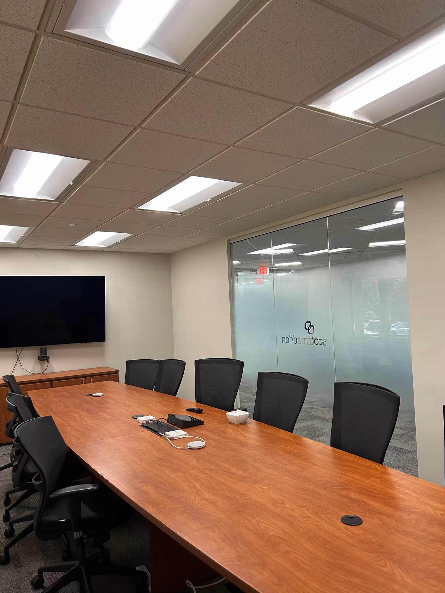 Conference room with a glass partition wall bearing a frosted graphic, set with a wood table and office chairs.
