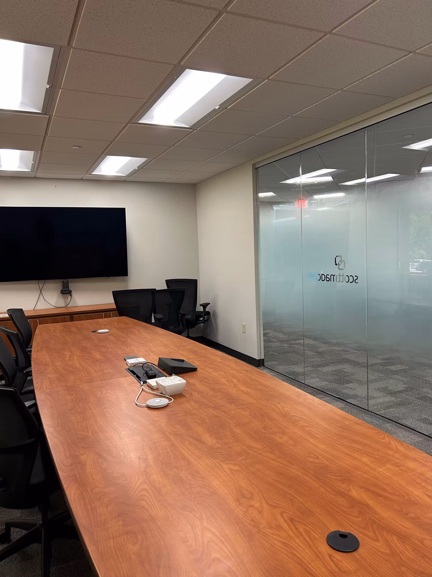 Boardroom glass partition with a frosted privacy band and cut-vinyl logo lettering beside a wall-mounted display and long meeting table.