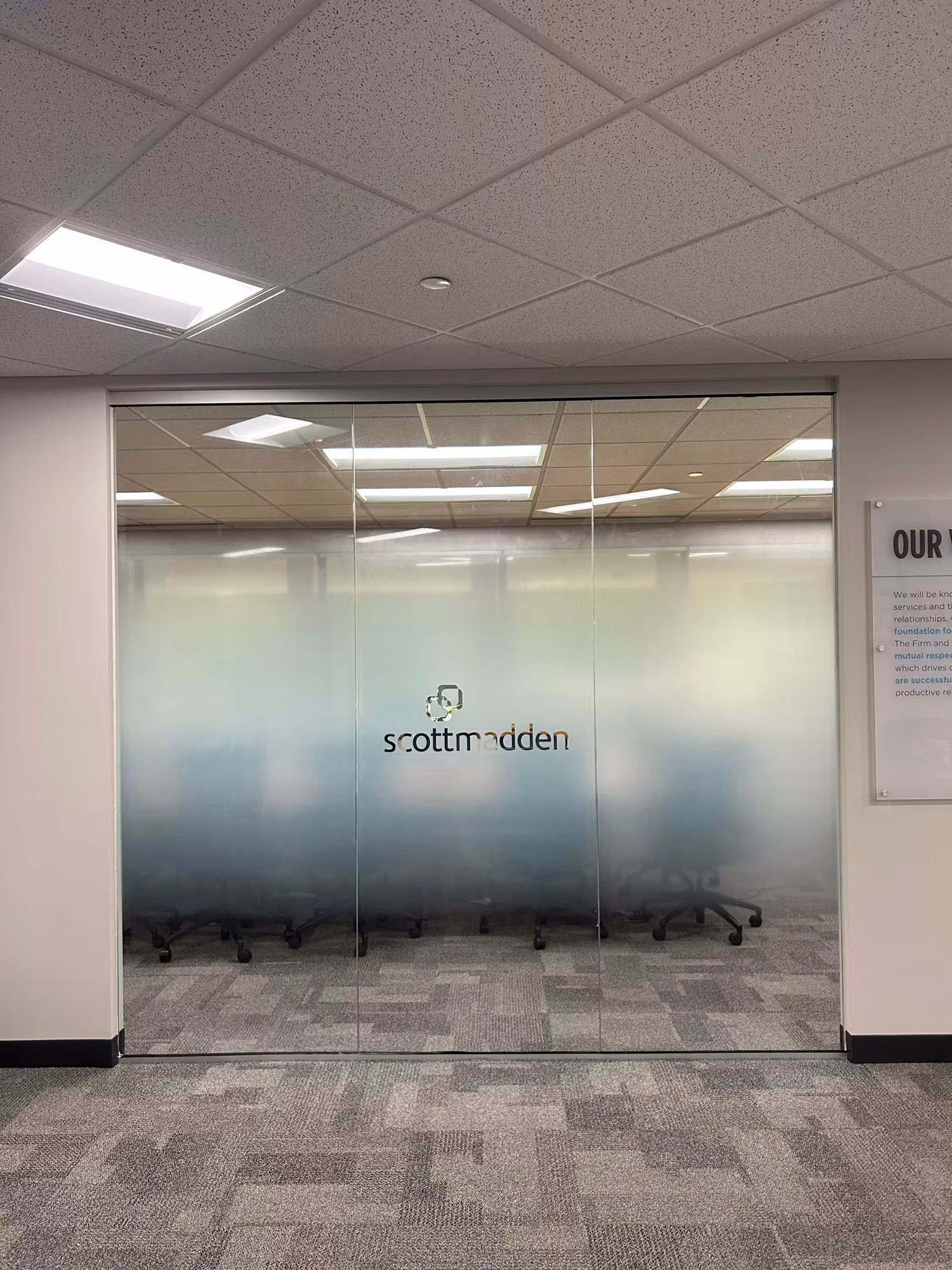Interior glass partition wall with a gradient frosted privacy band and centered cut-vinyl logo separating a meeting room from the corridor.