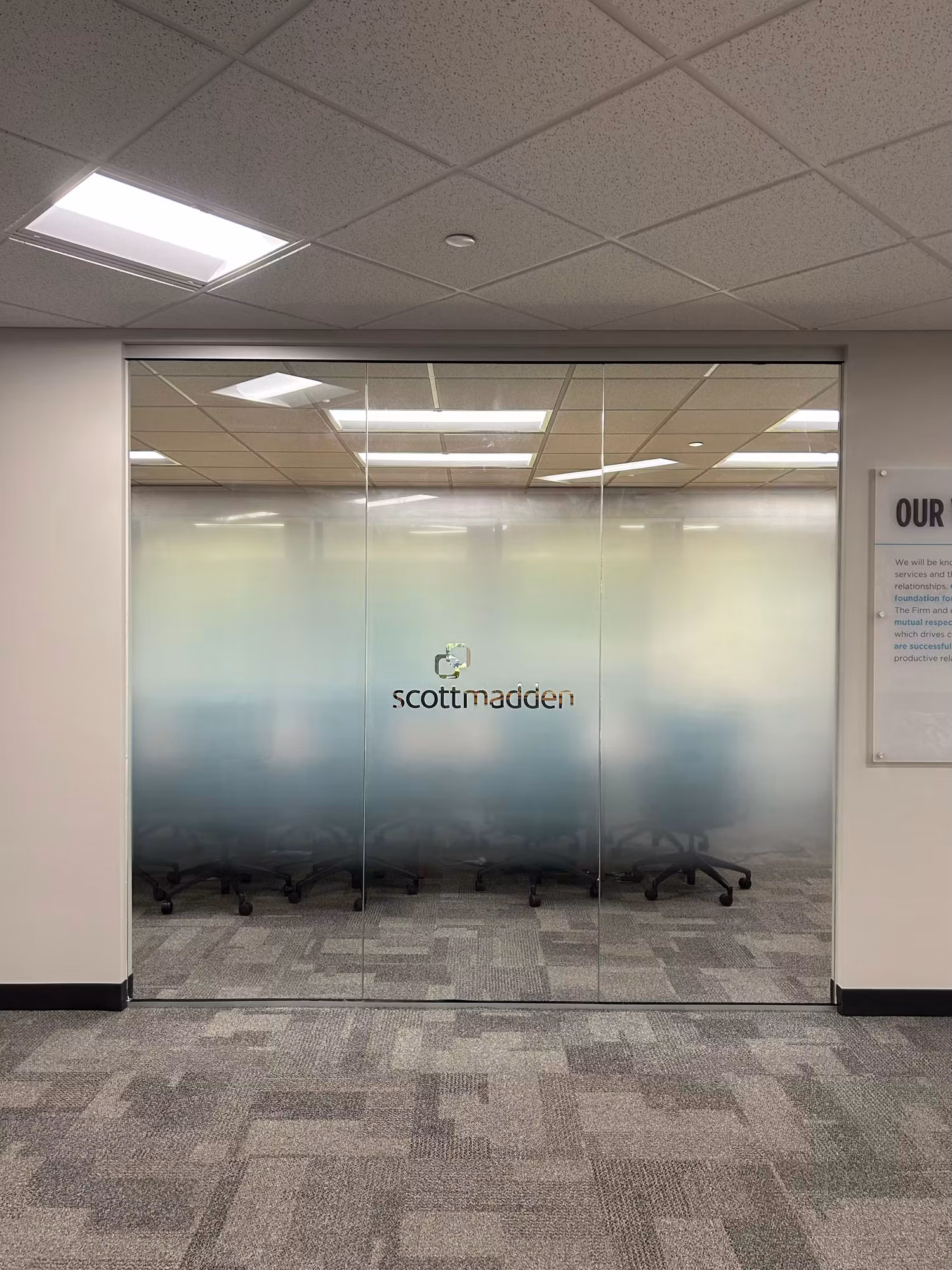 Office glass partition wall with a frosted privacy band and cut-vinyl logo lettering screening a conference room from the hallway.