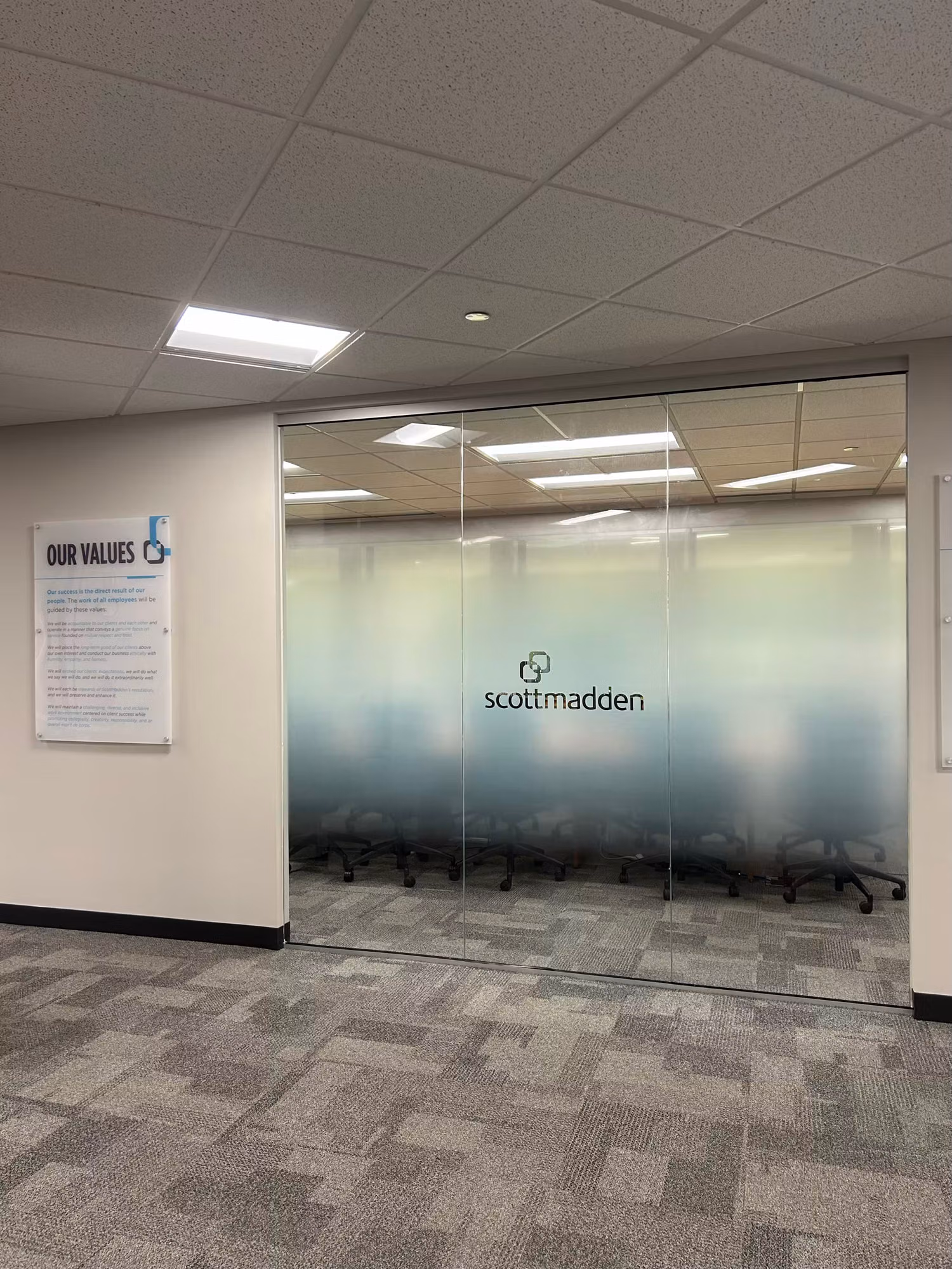 Glass-walled meeting room with a gradient frosted privacy band and cut-vinyl logo lettering viewed from the office corridor.