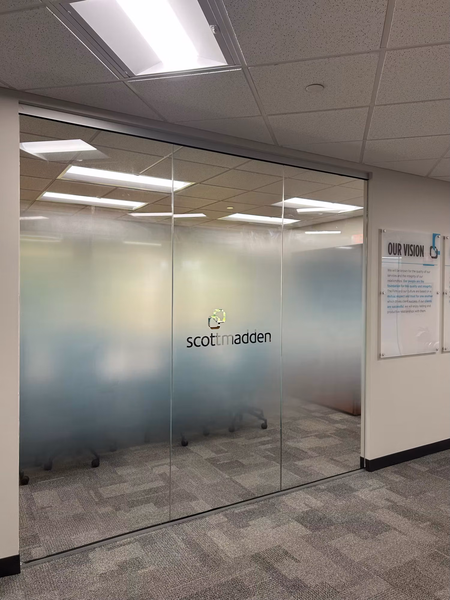 Interior glass partition with a gradient frosted privacy band and centered cut-vinyl logo lettering enclosing a conference room.
