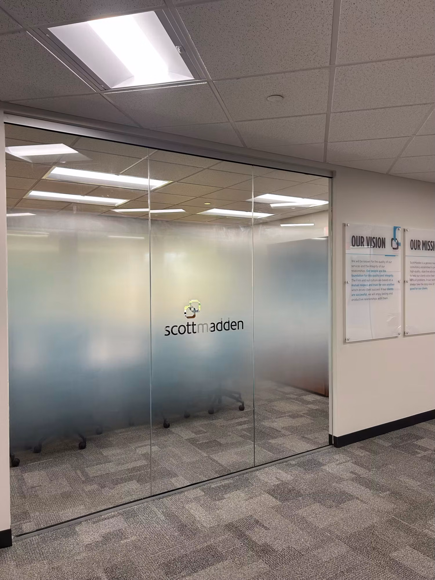 Glass conference room wall with a gradient frosted privacy band and cut-vinyl logo lettering seen from the corridor.