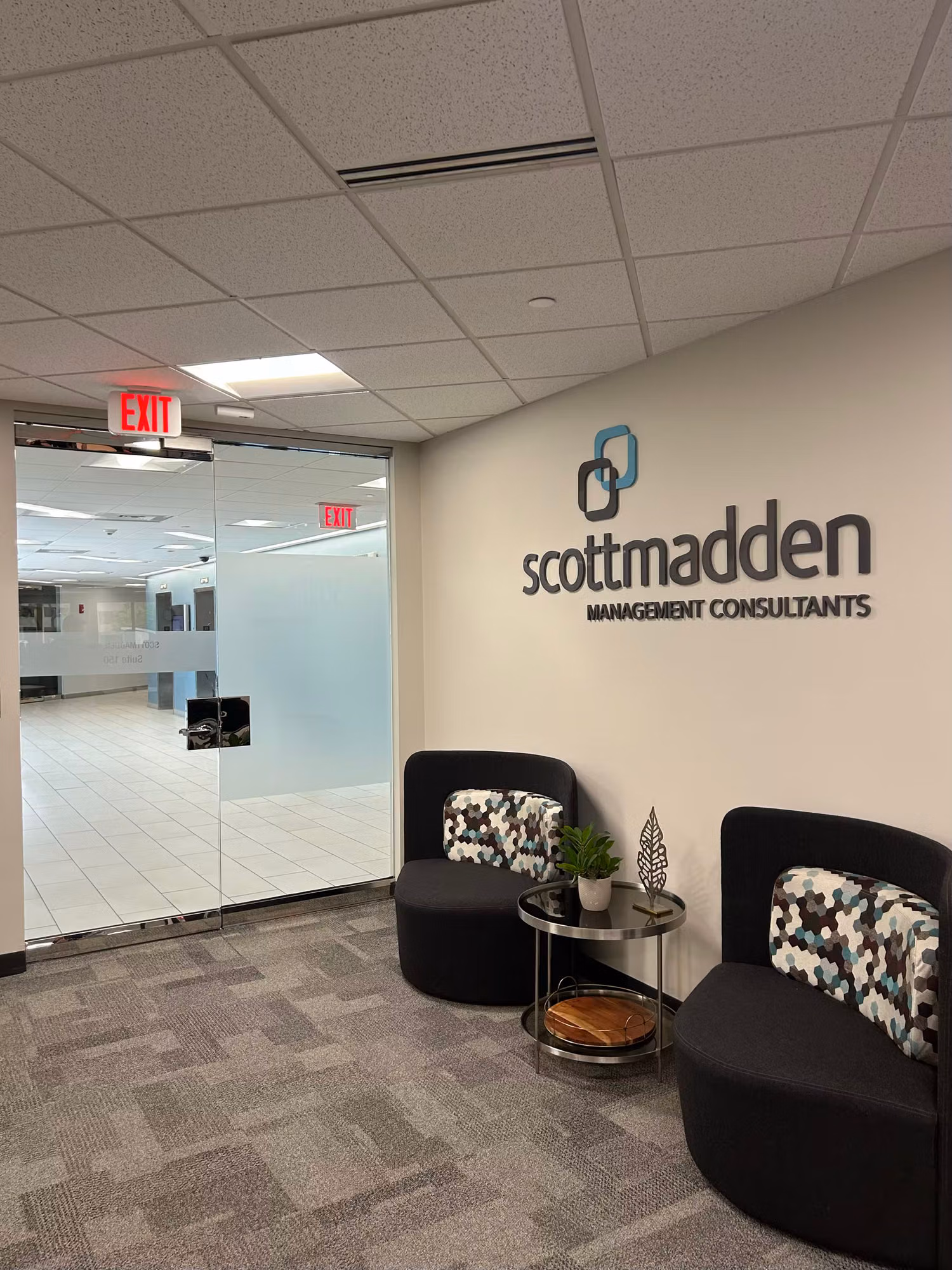 Office reception area with a frosted glass entry partition, dimensional wall lettering, and a small seating nook.