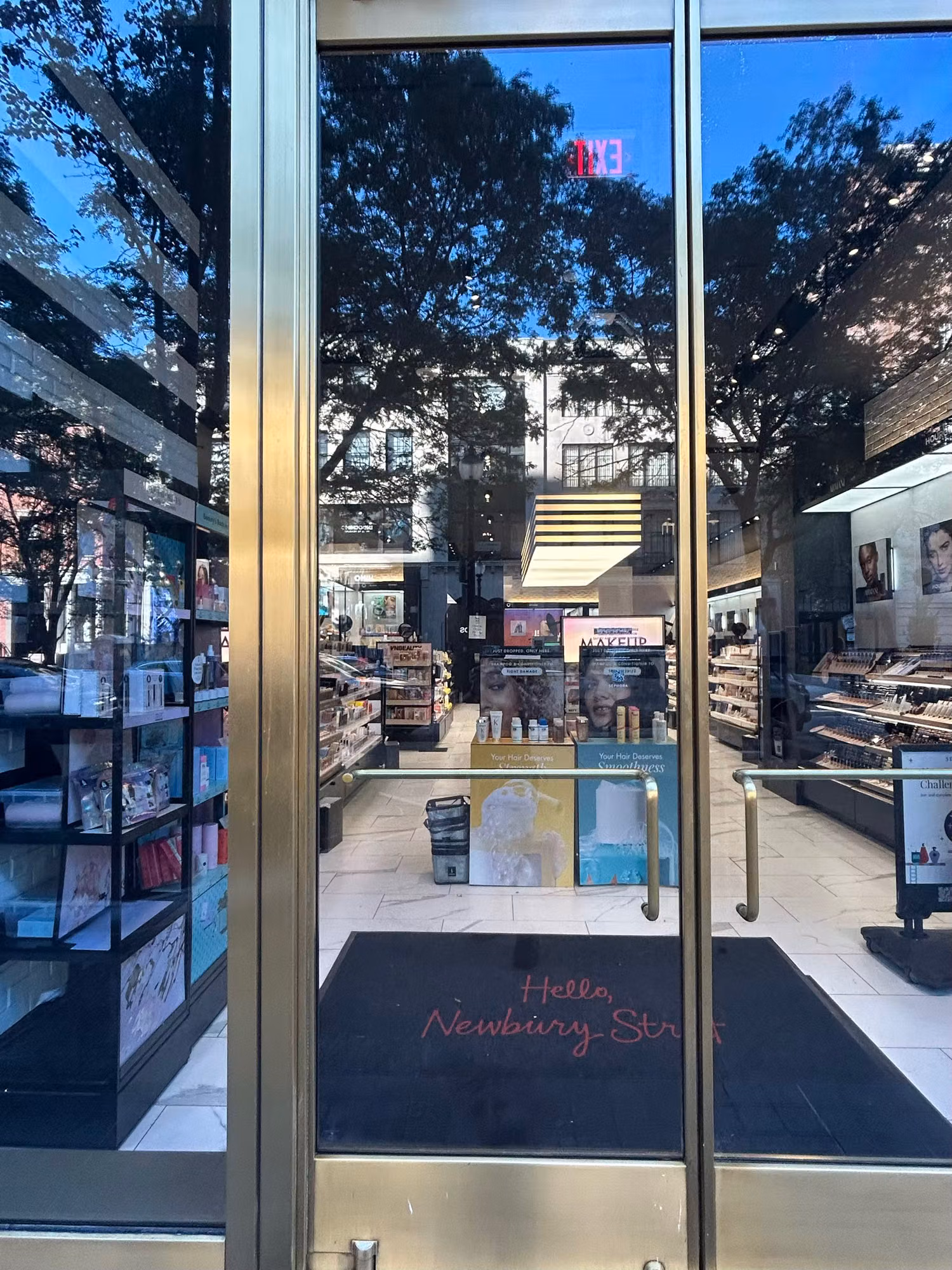 Glass storefront entry doors with brass framing leading into a cosmetics retail interior with display shelving.