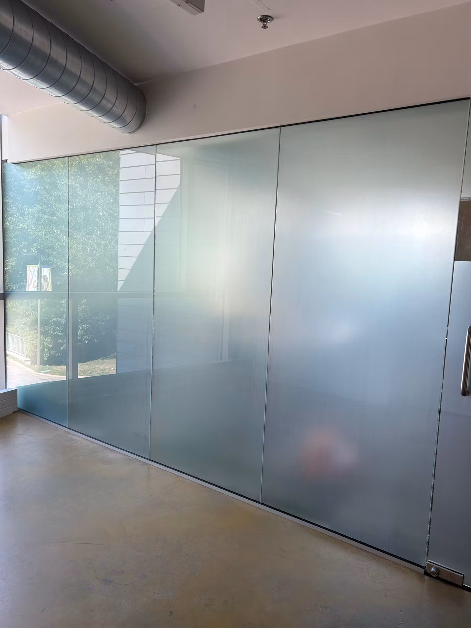 Floor-to-ceiling interior glass partition wall with frosted privacy film on lower panels and clear glass above.