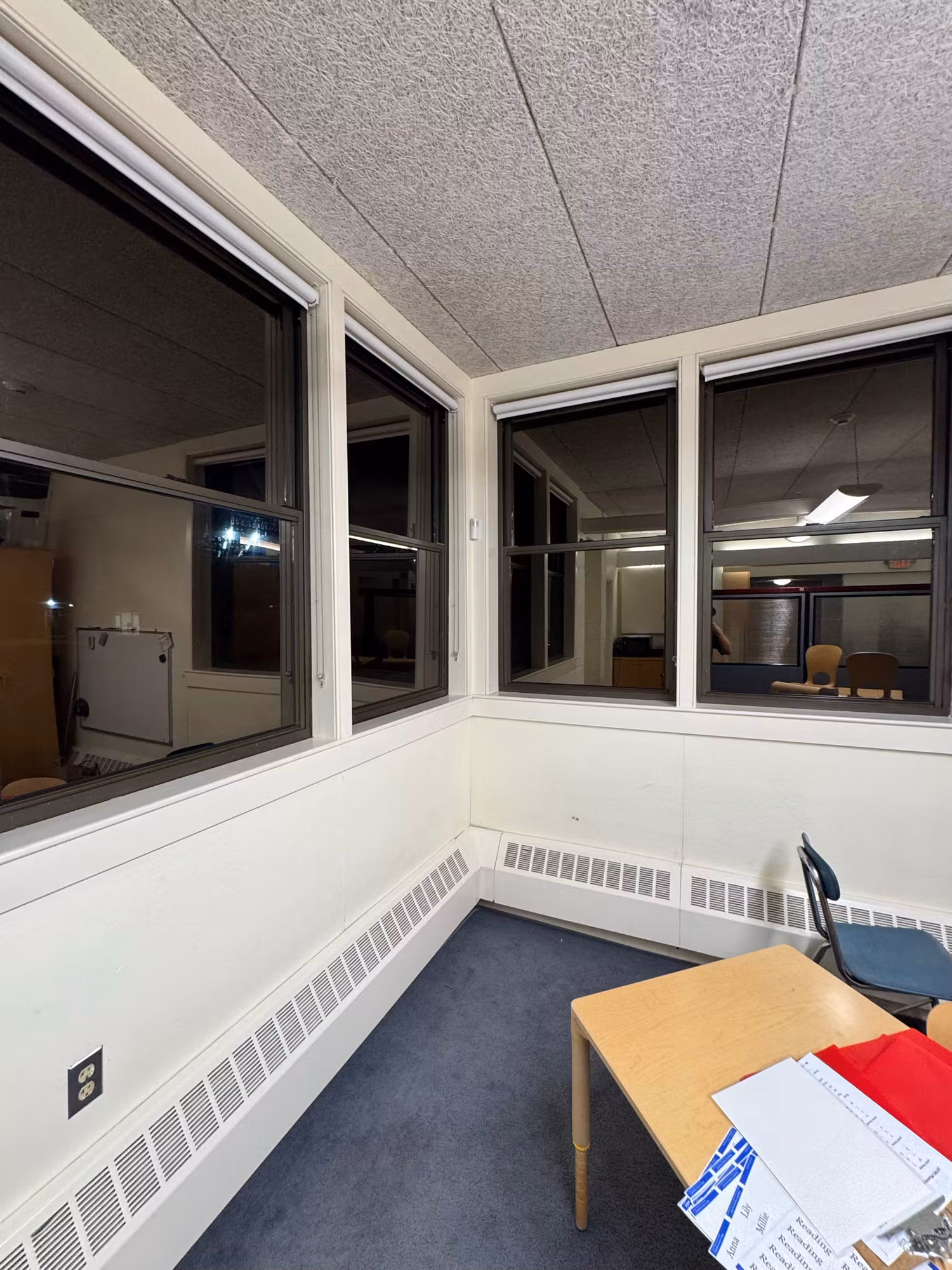 Interior office corner with partition windows looking into adjoining rooms, baseboard heaters and a desk below.