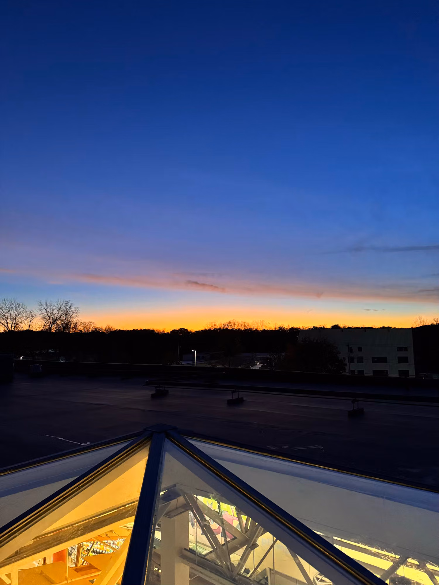 Pyramid glass skylight on a commercial rooftop glowing from interior light against a dusk sky.