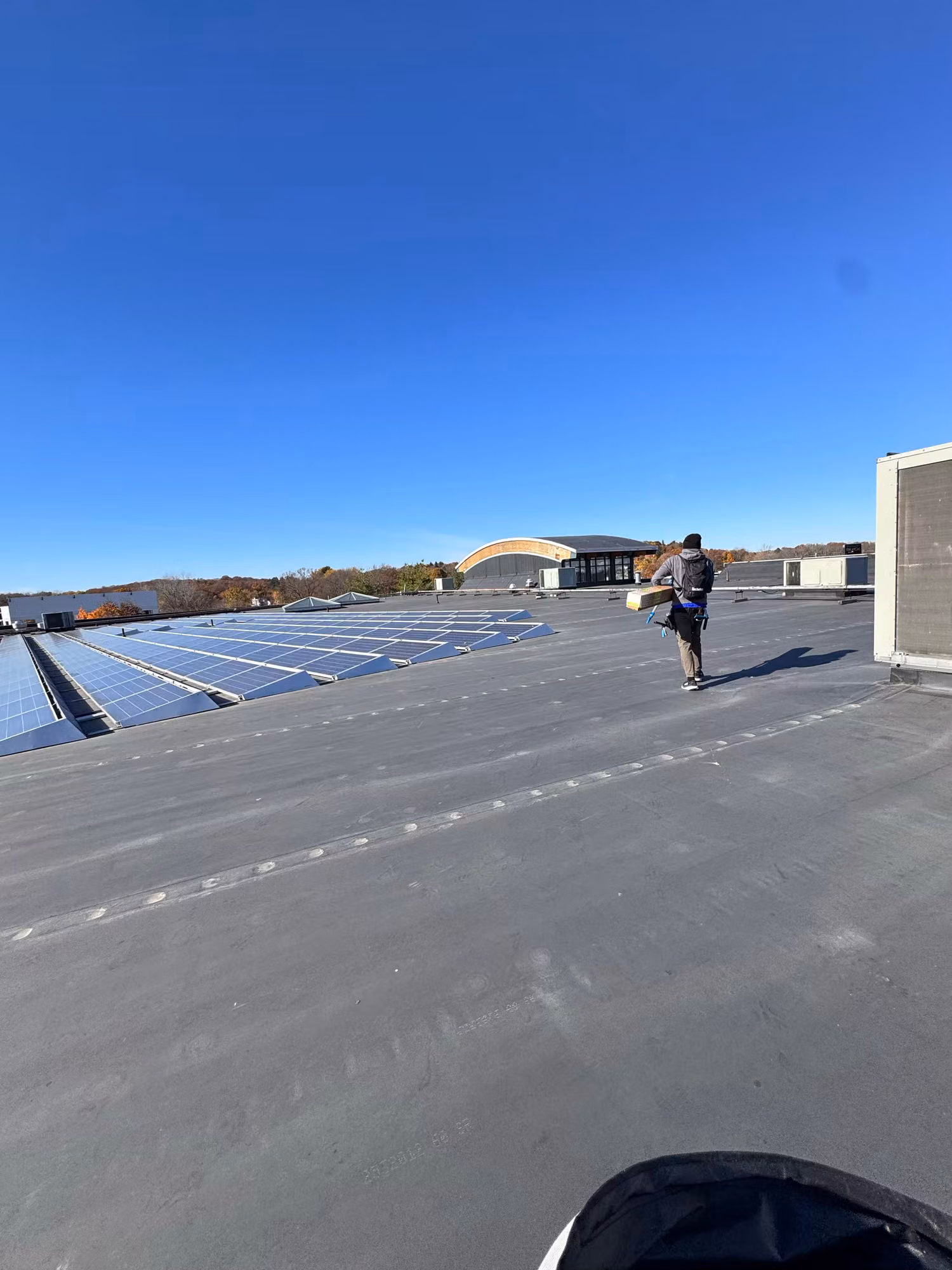 Worker carrying a roll across a flat commercial rooftop lined with rows of solar panels.