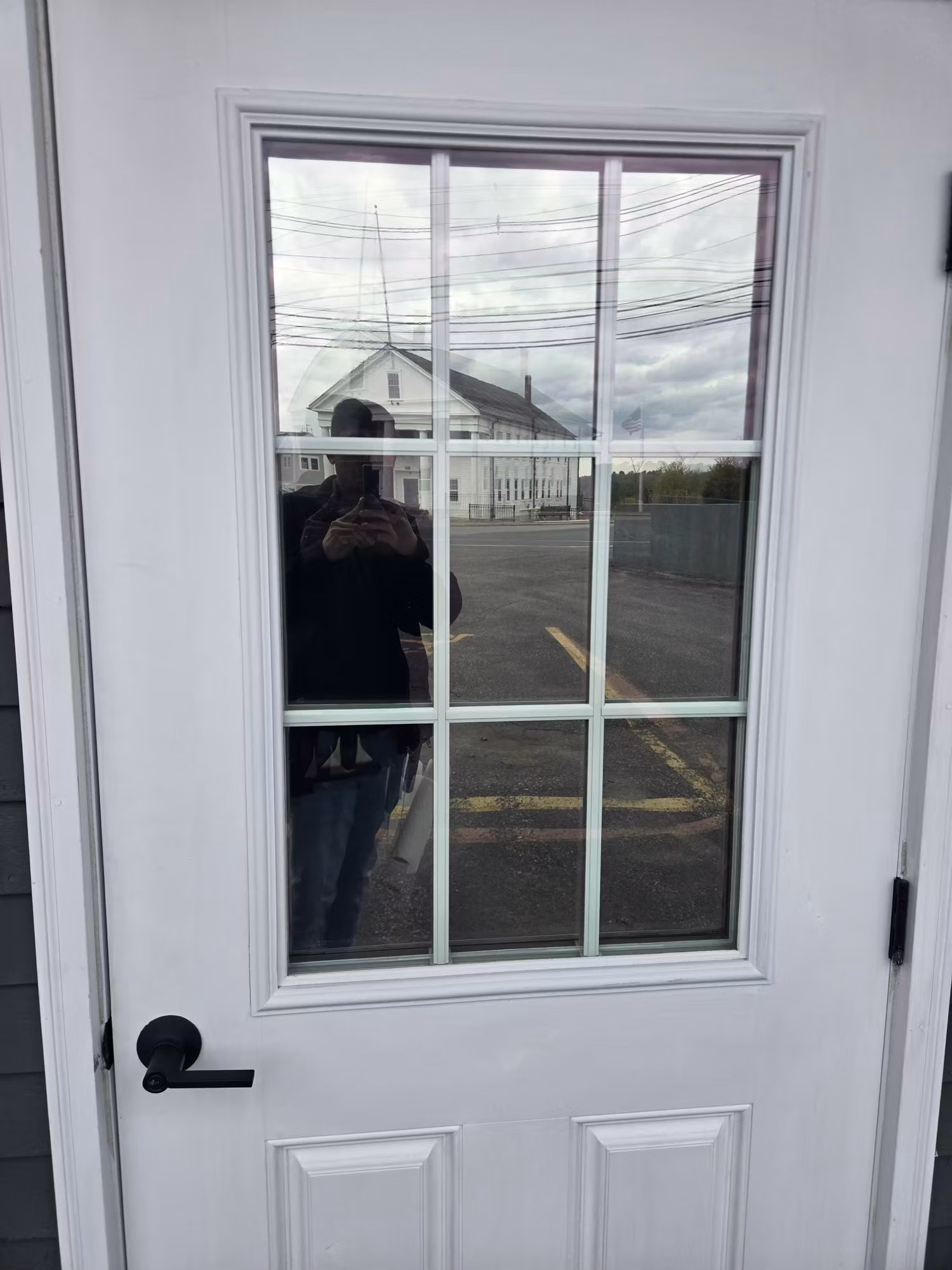 Close-up of a white entry door's divided-light glass panel with window film reflecting the lot and nearby building.