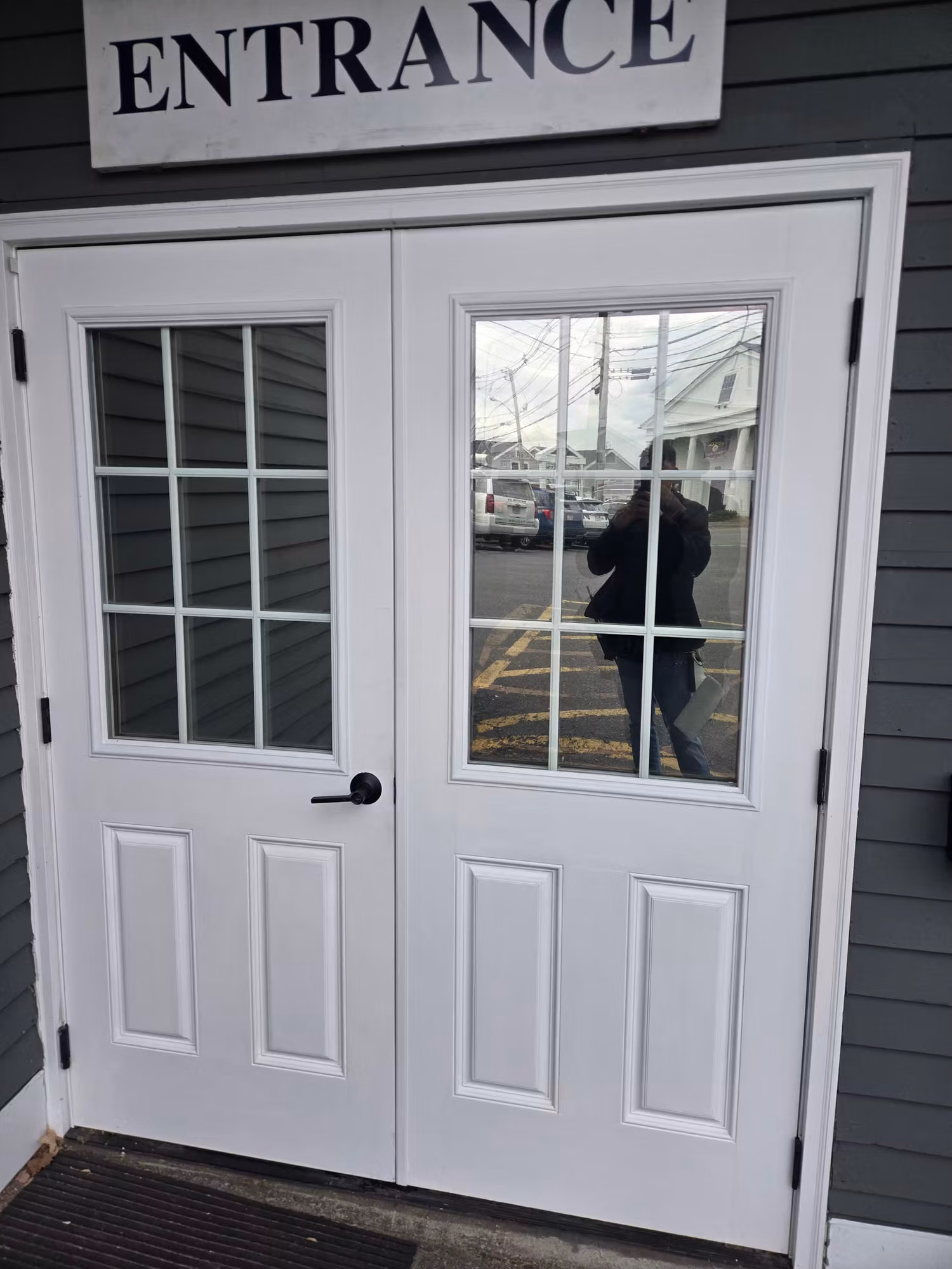 White double entry doors with divided-light glass panels treated with window film, reflecting the parking lot.