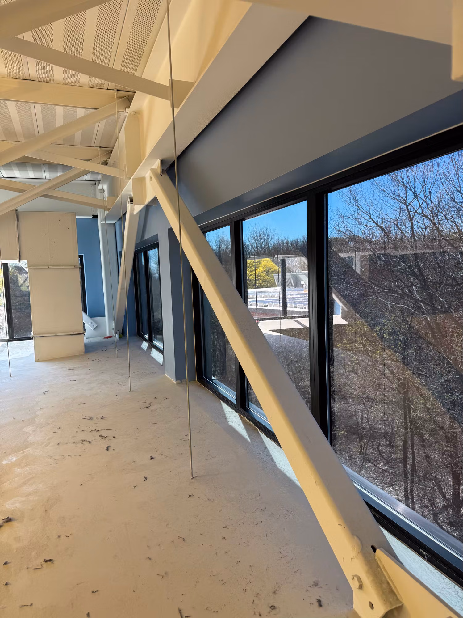 Upper-floor room with an angled wall of large windows facing wooded grounds during building fit-out.