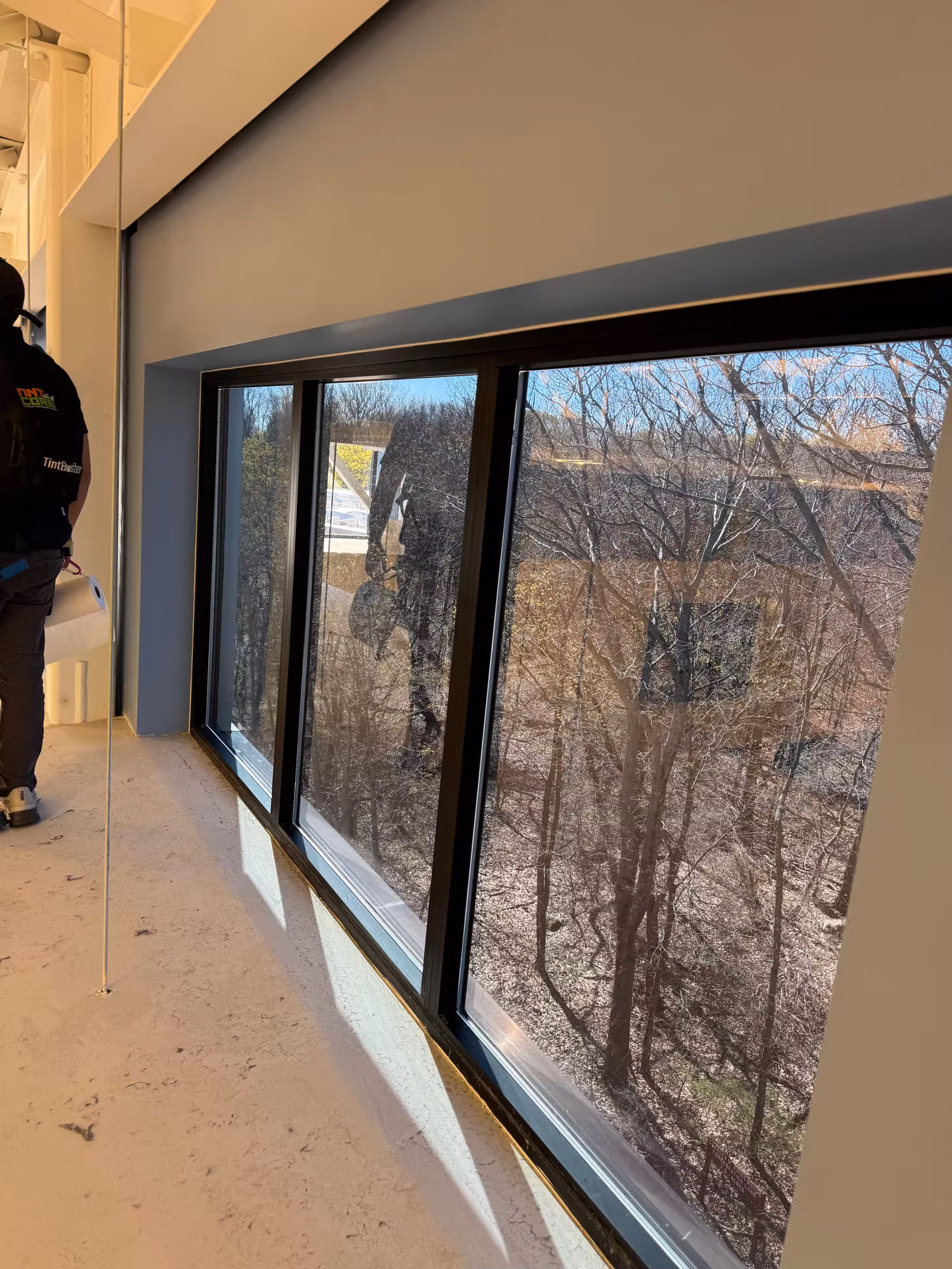 Installer working along a long corridor window wall overlooking a winter tree line during fit-out.