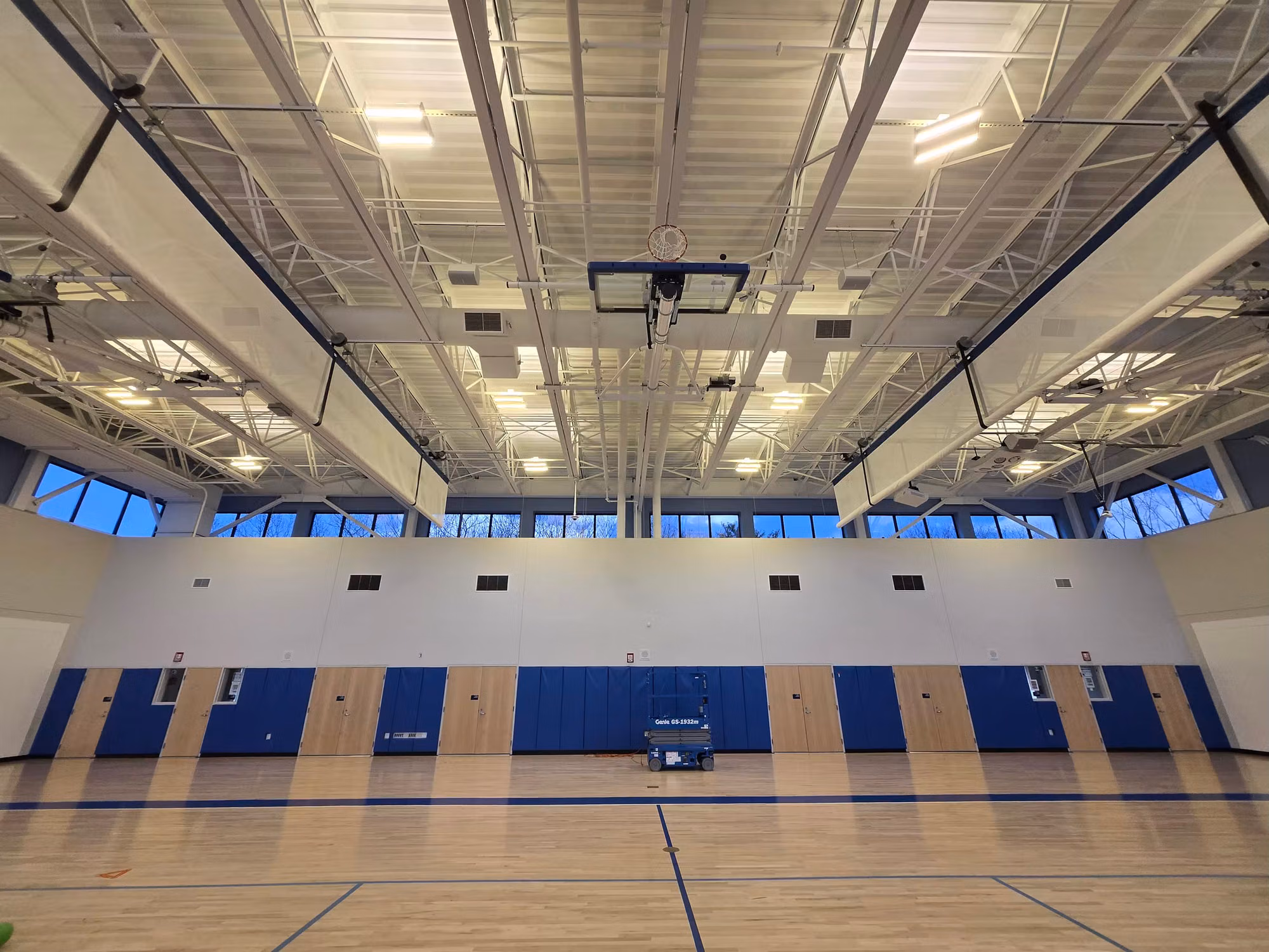 School gymnasium interior with a row of upper clerestory windows above the wall padding and maple court.