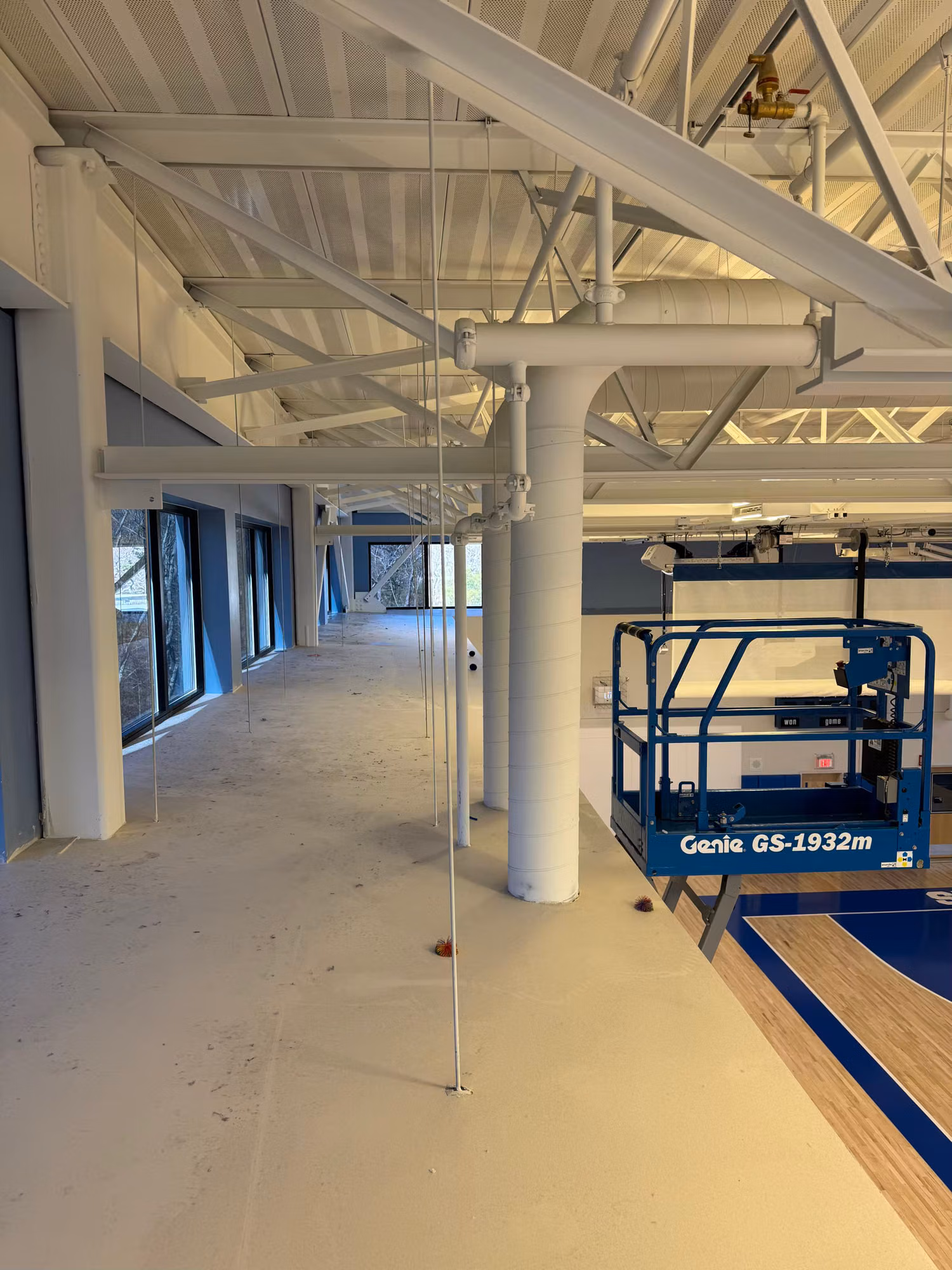 Commercial interior during fit-out with a Genie lift positioned near a wall of windows ready for film installation.