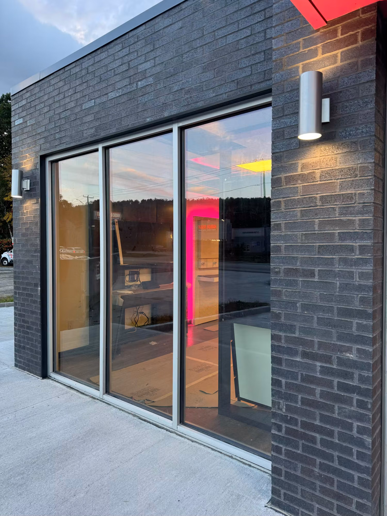 Corner storefront windows on a dark brick retail building with reflective glass catching street reflections at dusk.