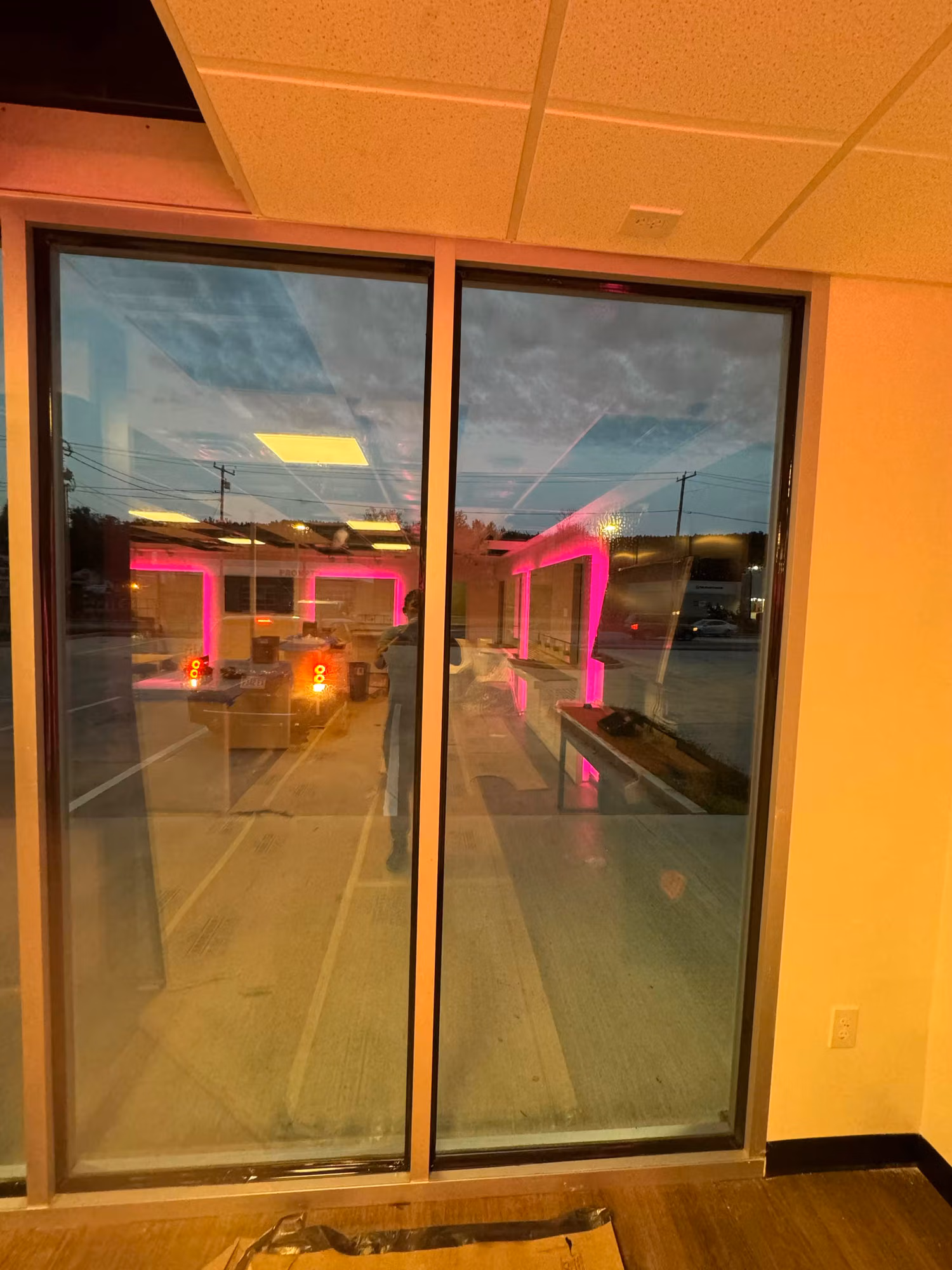 Interior view through a large storefront window wall looking out to the parking lot at dusk.