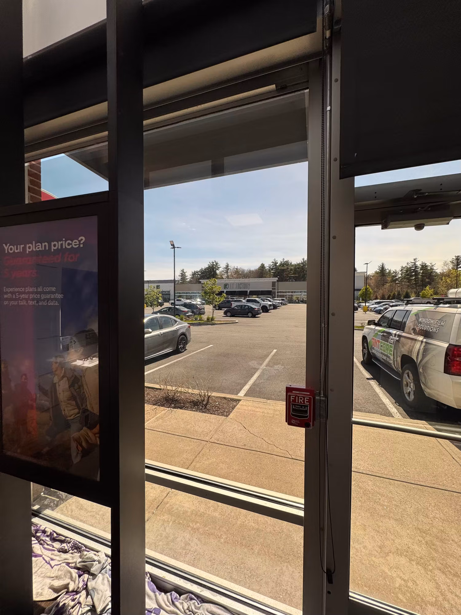 Interior view through a large storefront window looking out across a parking lot toward neighboring buildings.