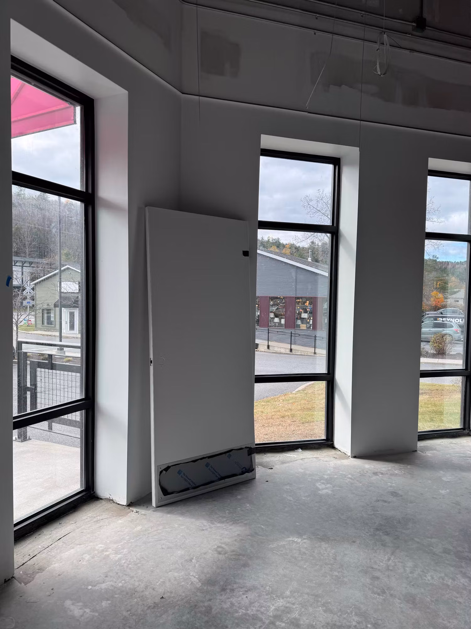 Commercial interior under buildout with a row of floor-to-ceiling storefront windows looking out to a street and lot.