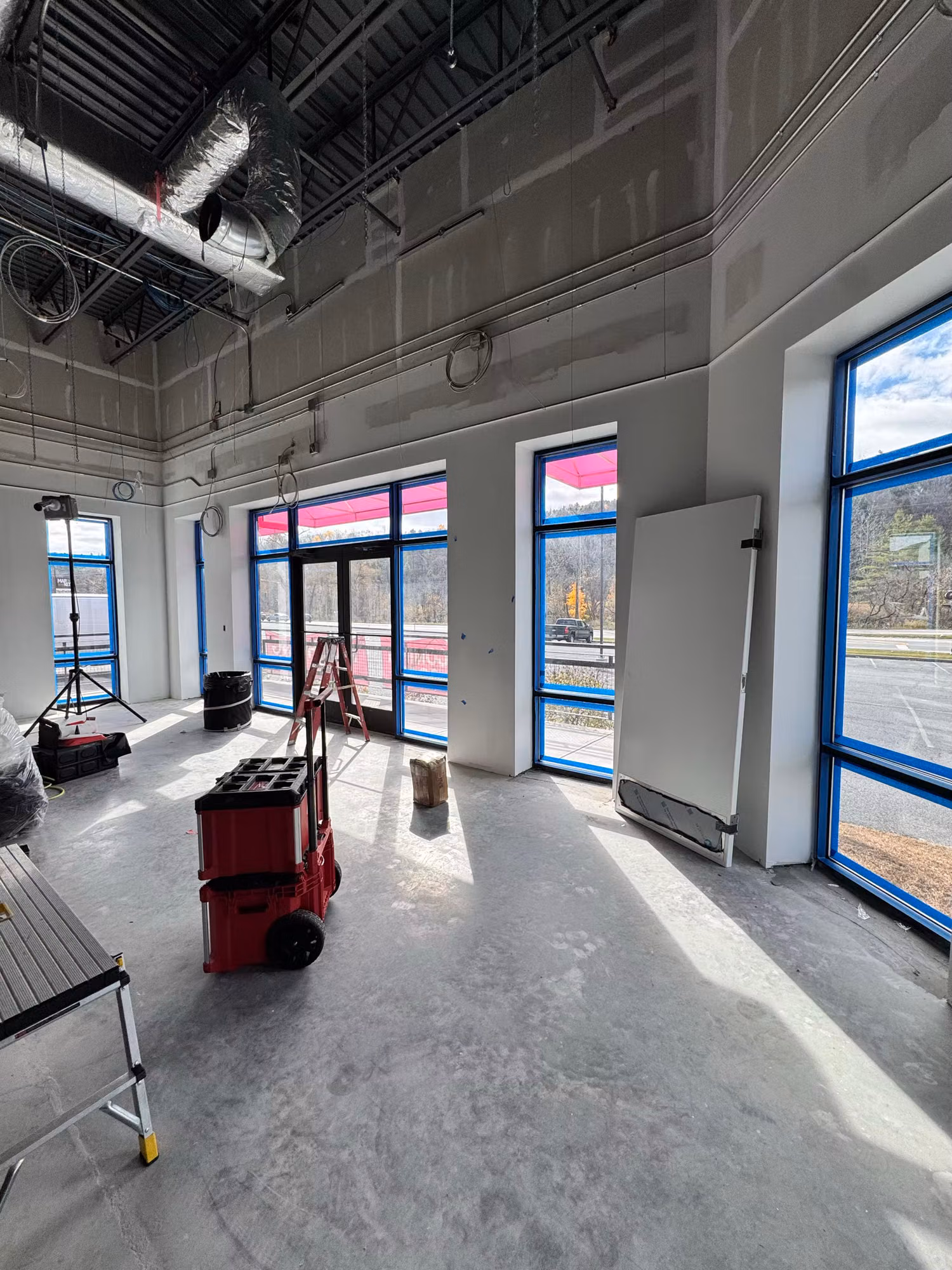Interior of a commercial retail space under buildout with floor-to-ceiling storefront windows and glass entry doors.