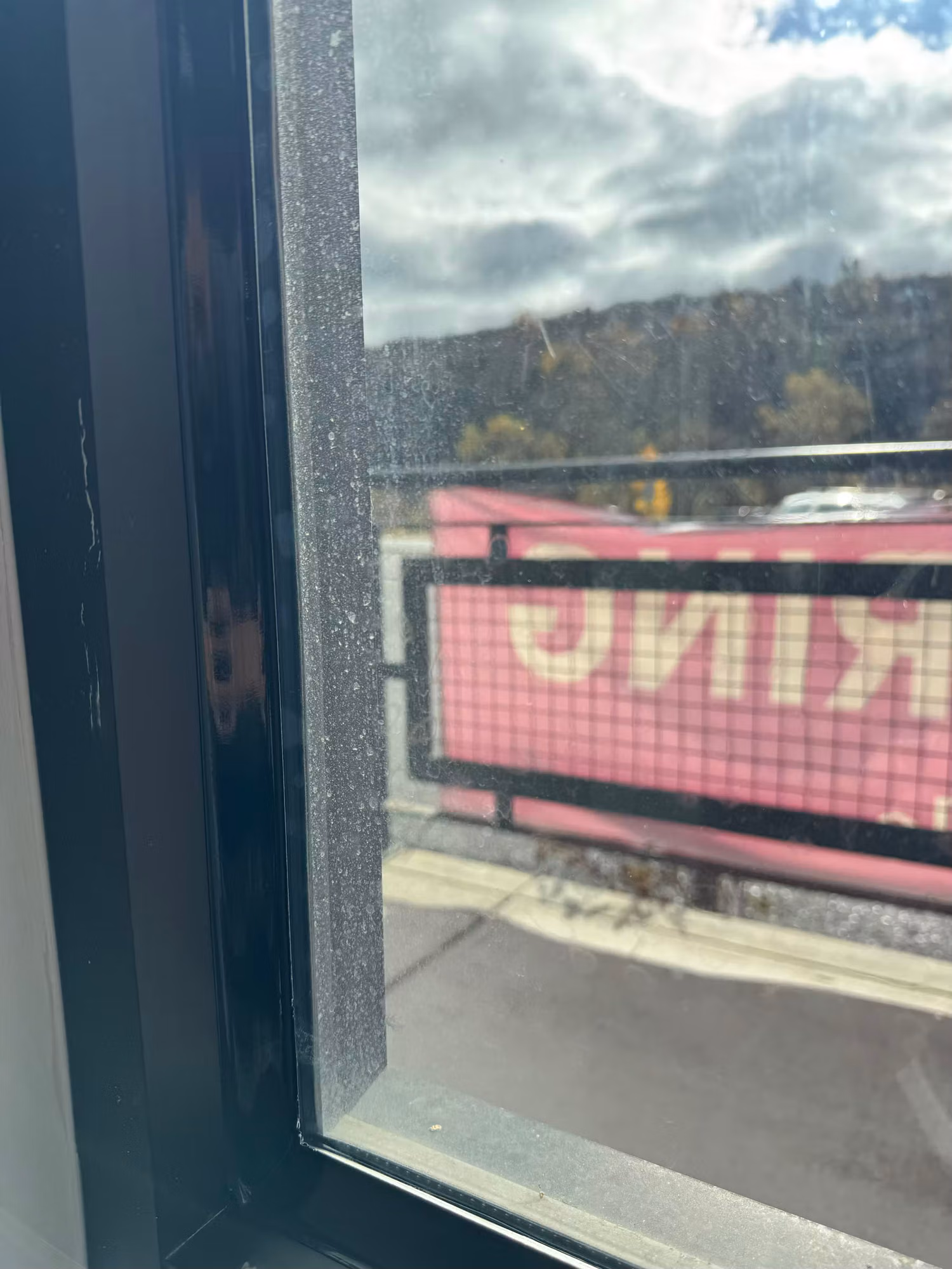 Close-up of a commercial storefront window frame and clear glass looking out toward a parking lot.