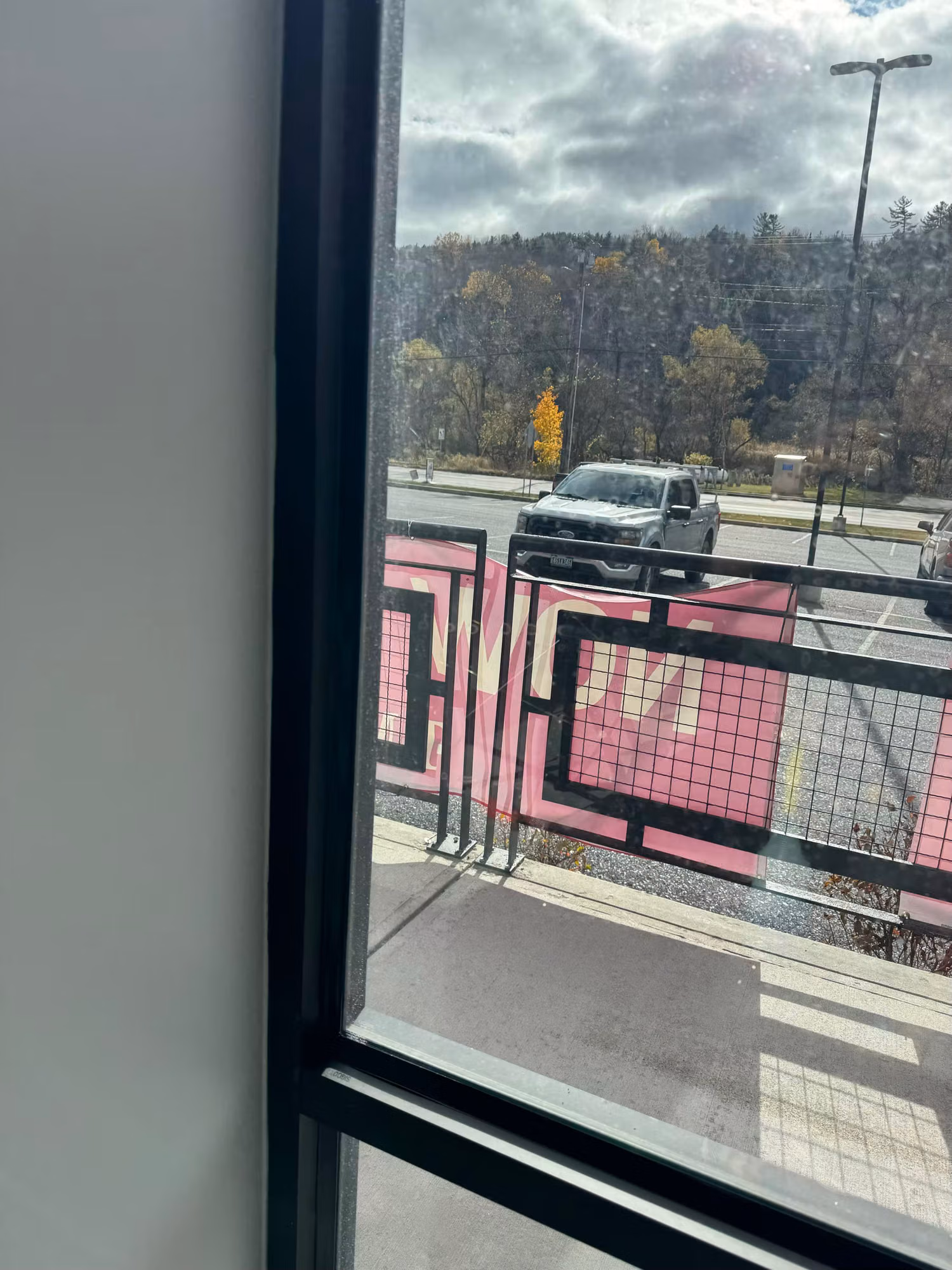 View through a clear commercial storefront window toward a parking area with a parked truck and railing.