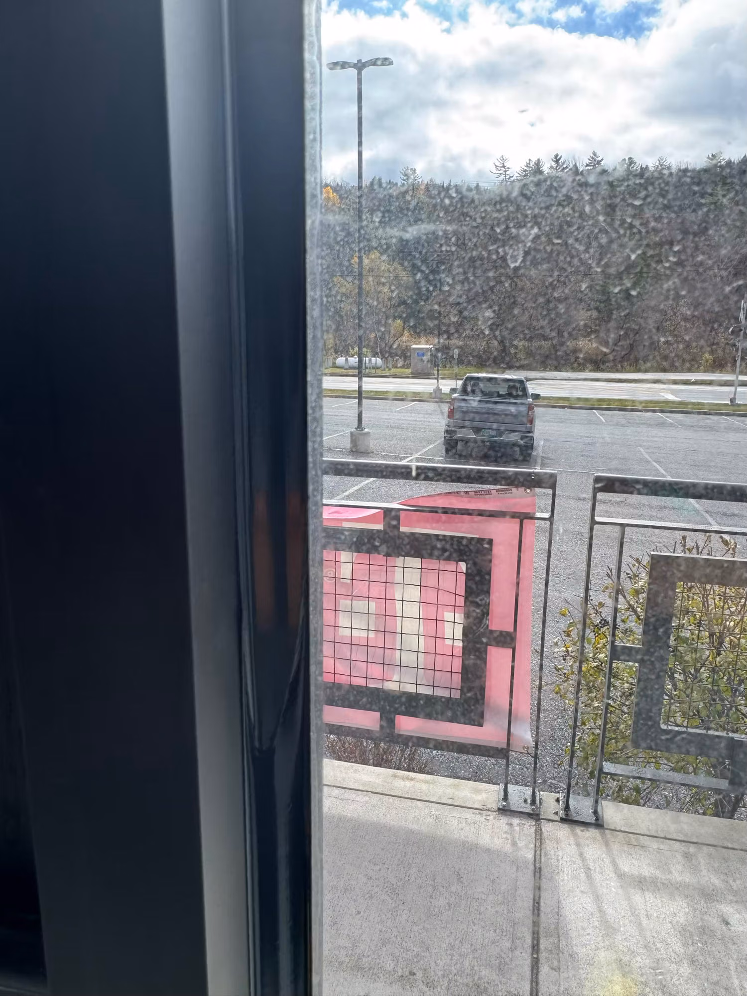 Close-up through a clear commercial storefront window looking out over a paved lot and hillside.
