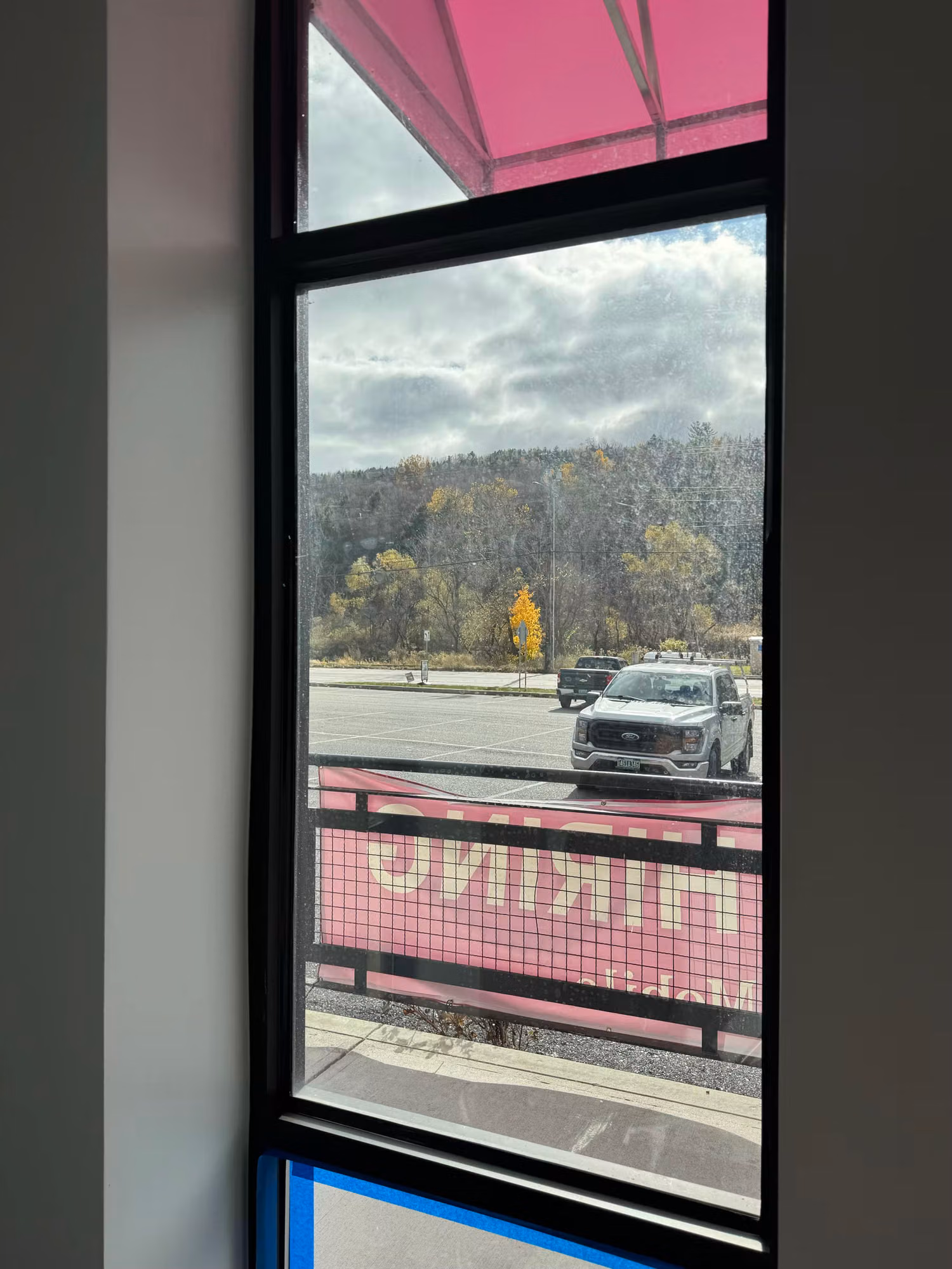 Tall commercial storefront window with clear glass framing a view of the parking lot and a parked truck.