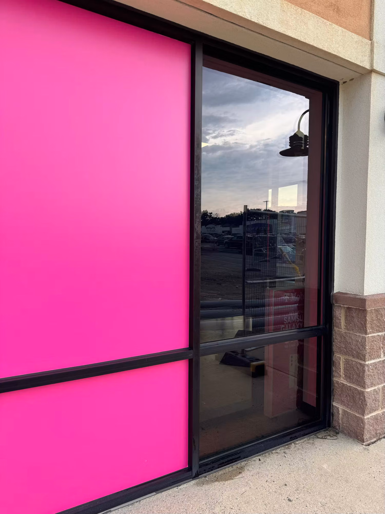 Retail storefront window with a solid magenta decorative film panel beside a clear glass entry door.