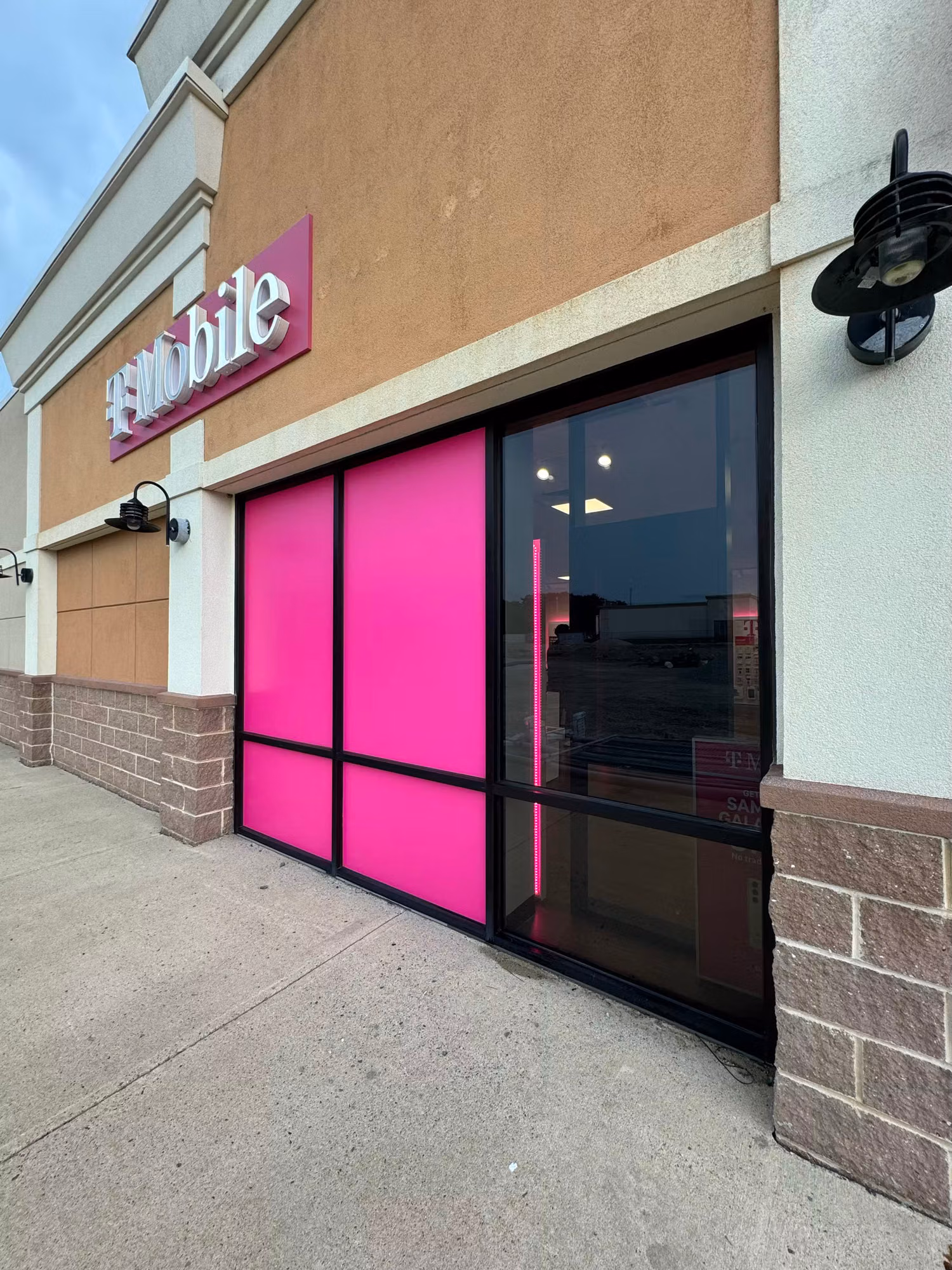 Retail storefront entry with magenta decorative film panels framing a clear glass door under a lit sign.