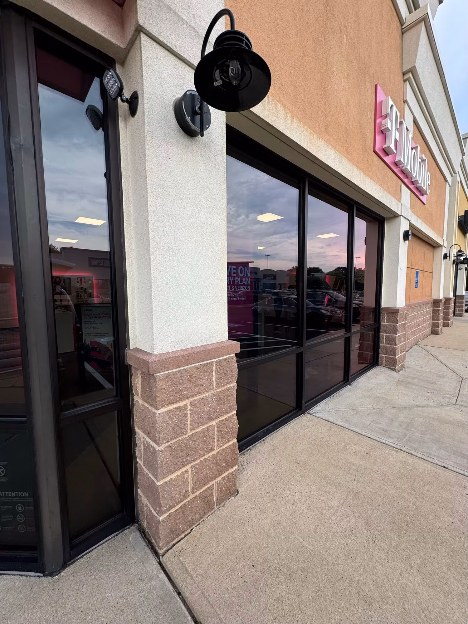 Angled view of darkly tinted retail storefront windows along a sidewalk with a stone-faced column.